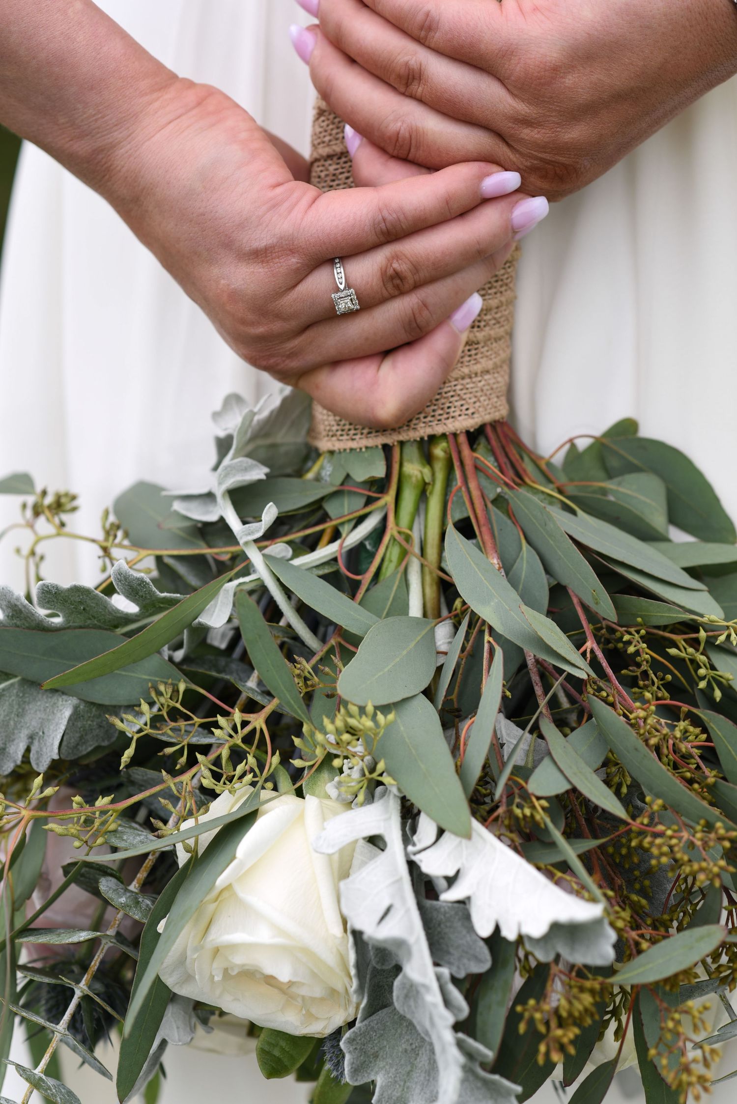 Close-up of hands holding a bridal bouquet with white roses and eucalyptus leaves.