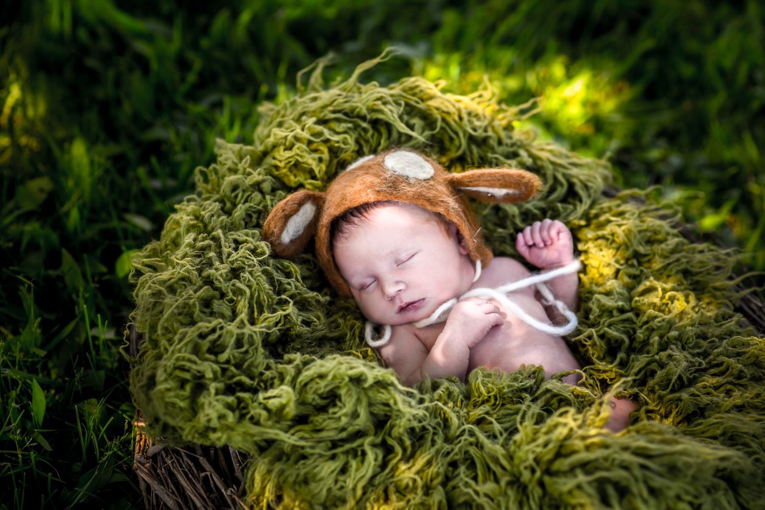 Sleeping baby wearing bunny ears rests peacefully on soft green mossy bedding in an outdoor setting.