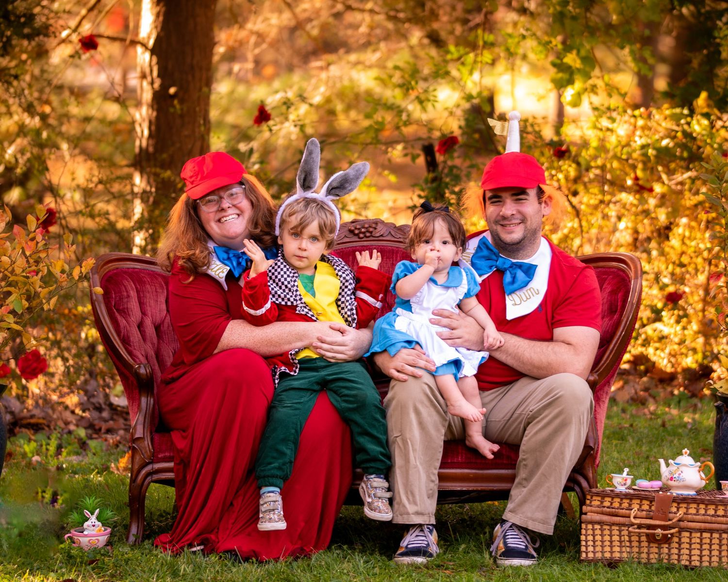 Family group in coordinating outfits sits together on red couch outdoors during autumn photoshoot.