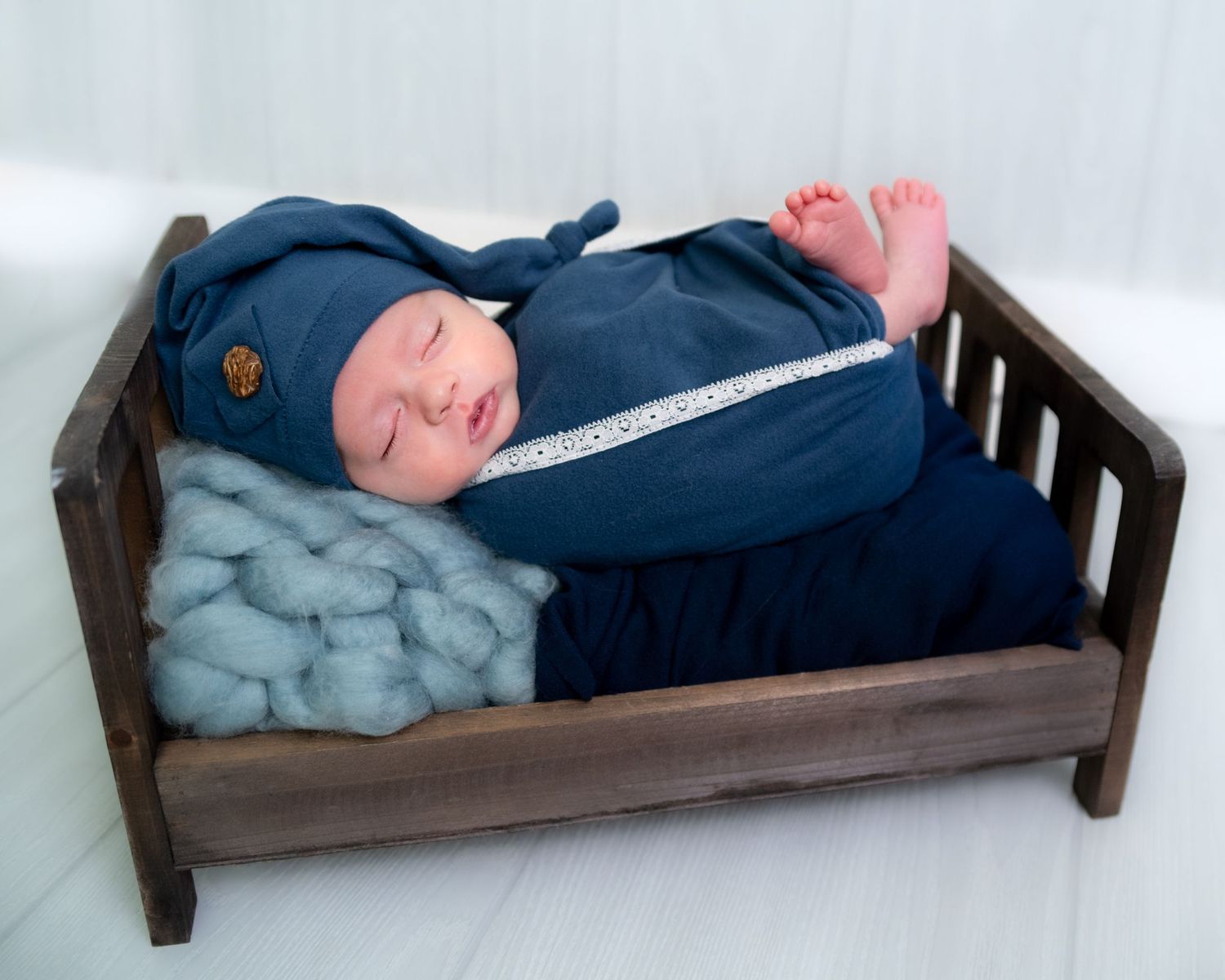 A small wooden doll bed with blue bedding shown from multiple angles.
