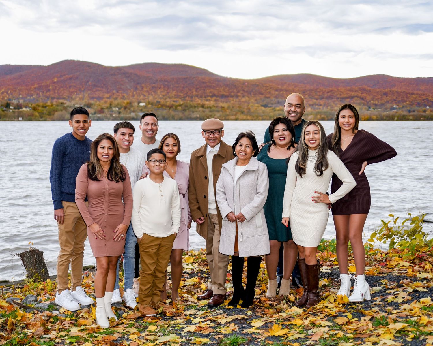 A group poses together on a rocky beach with autumn foliage and mountains in the background during fall season.