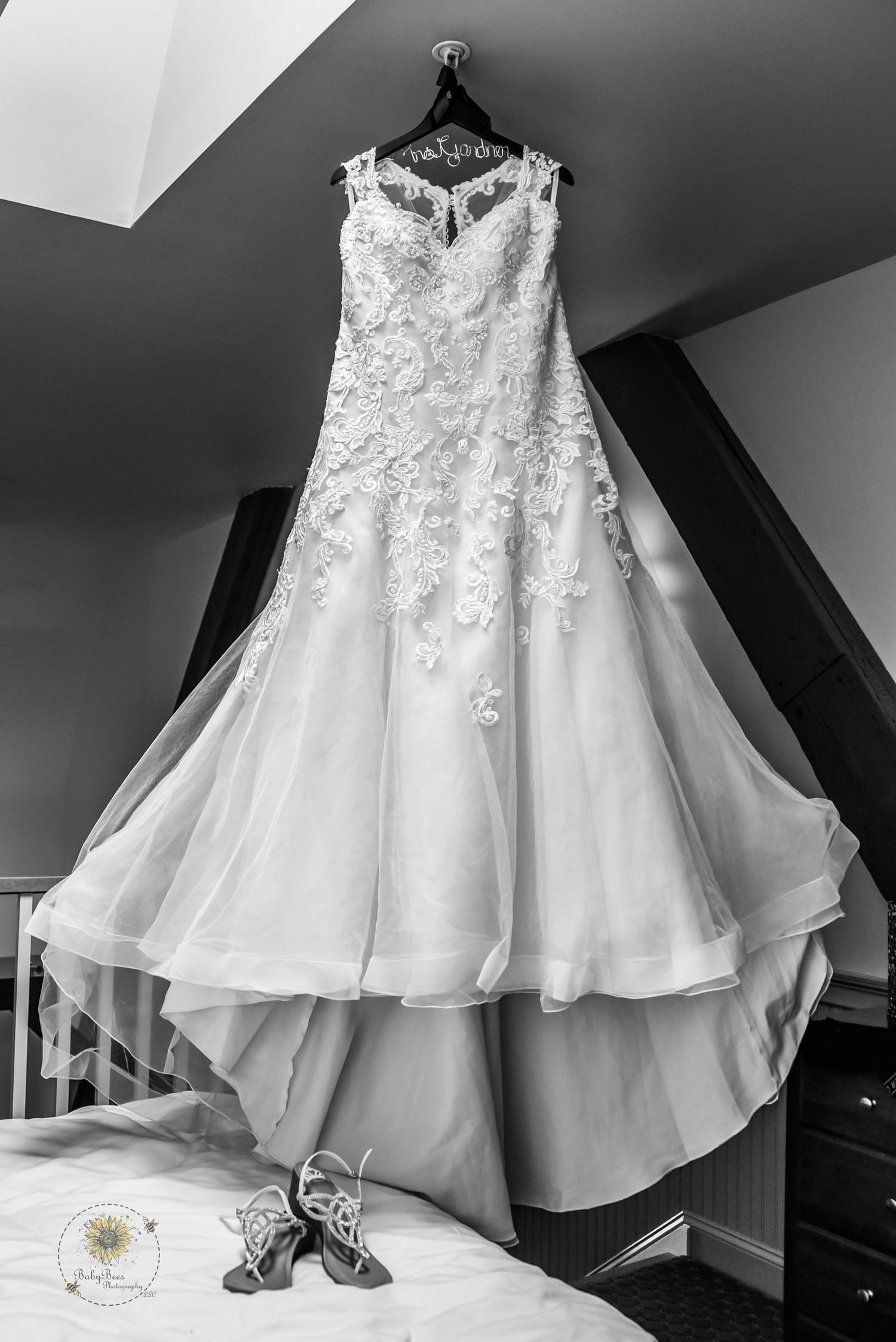 Elegant white lace wedding dress with layered tulle skirt hanging against dark wall.