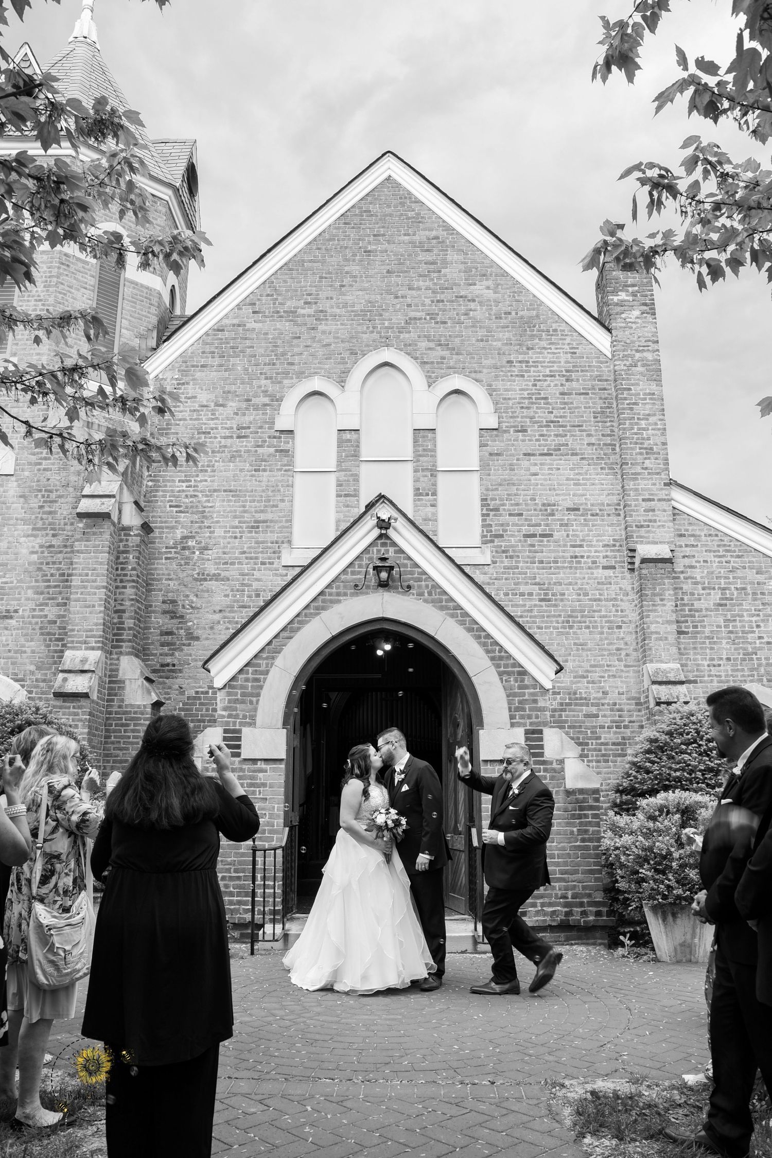 Black and white photo of wedding ceremony outside historic brick church with gothic architecture.