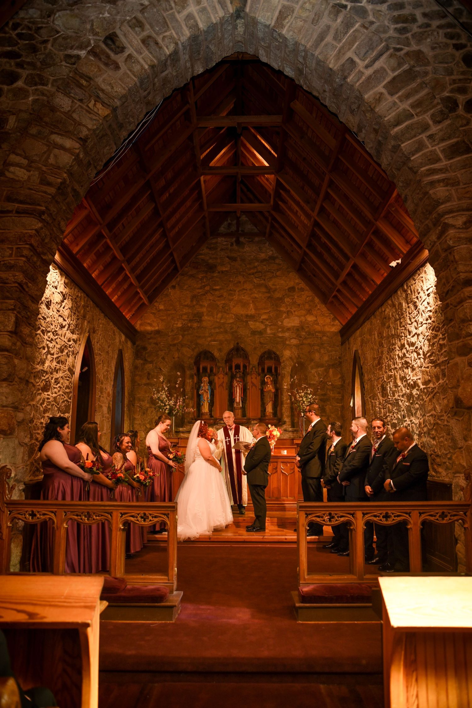 Wedding ceremony in candlelit stone chapel with exposed wooden beams.
