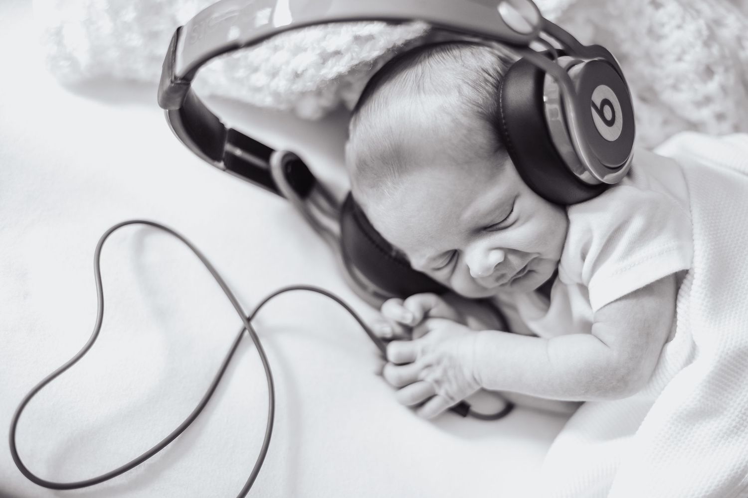 A sleeping baby wearing large black headphones lies peacefully on white bedding.