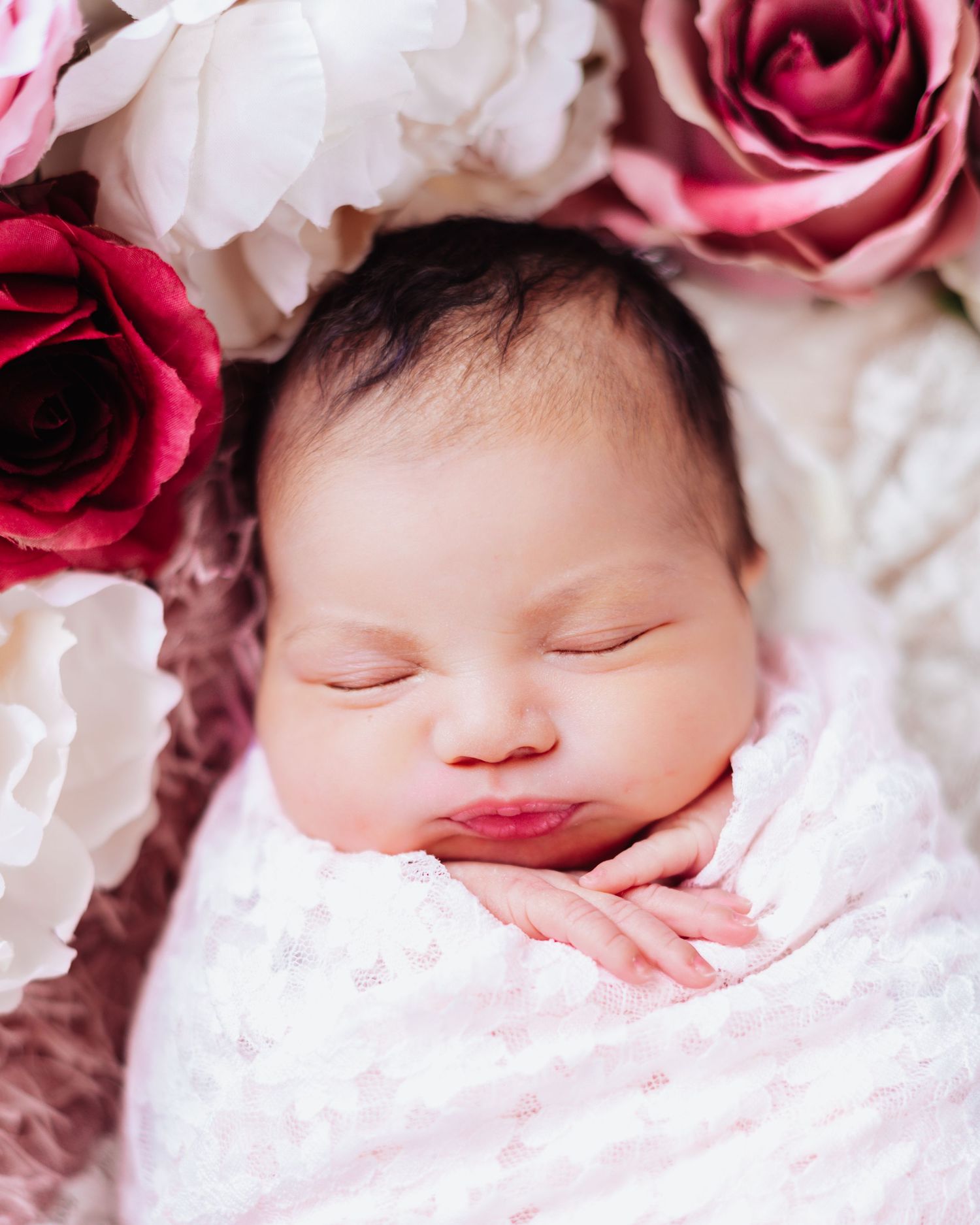 Sleeping newborn wrapped in pink blanket surrounded by pink and white roses.