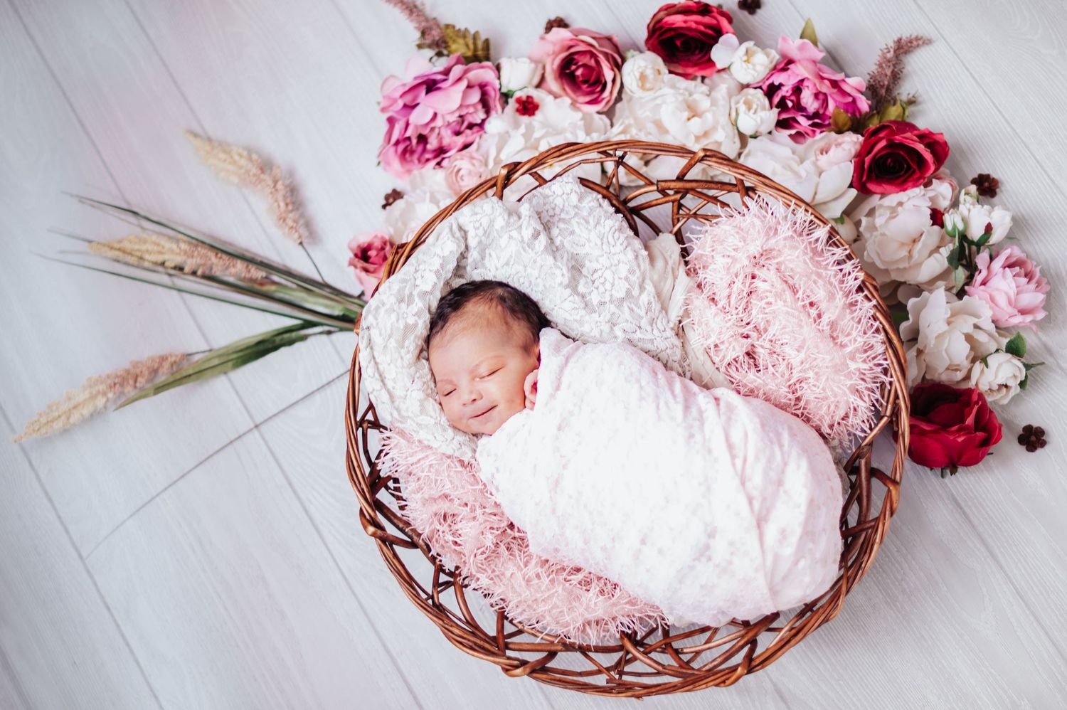 Delicate pink and red floral arrangements with dried elements surrounding a handmade ceramic bowl on white surface.