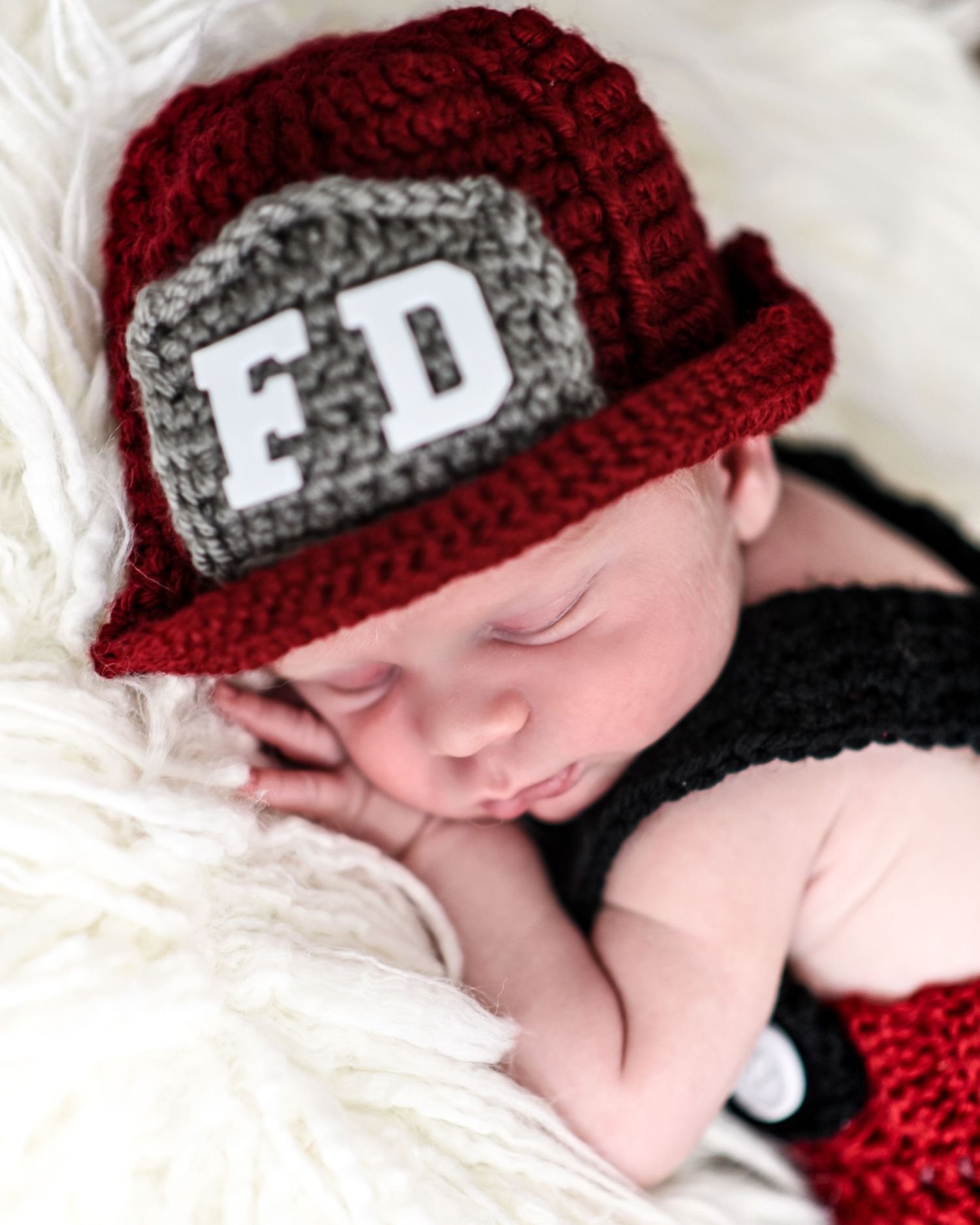 A sleeping baby wearing a red and gray crocheted beanie hat lies on white bedding.