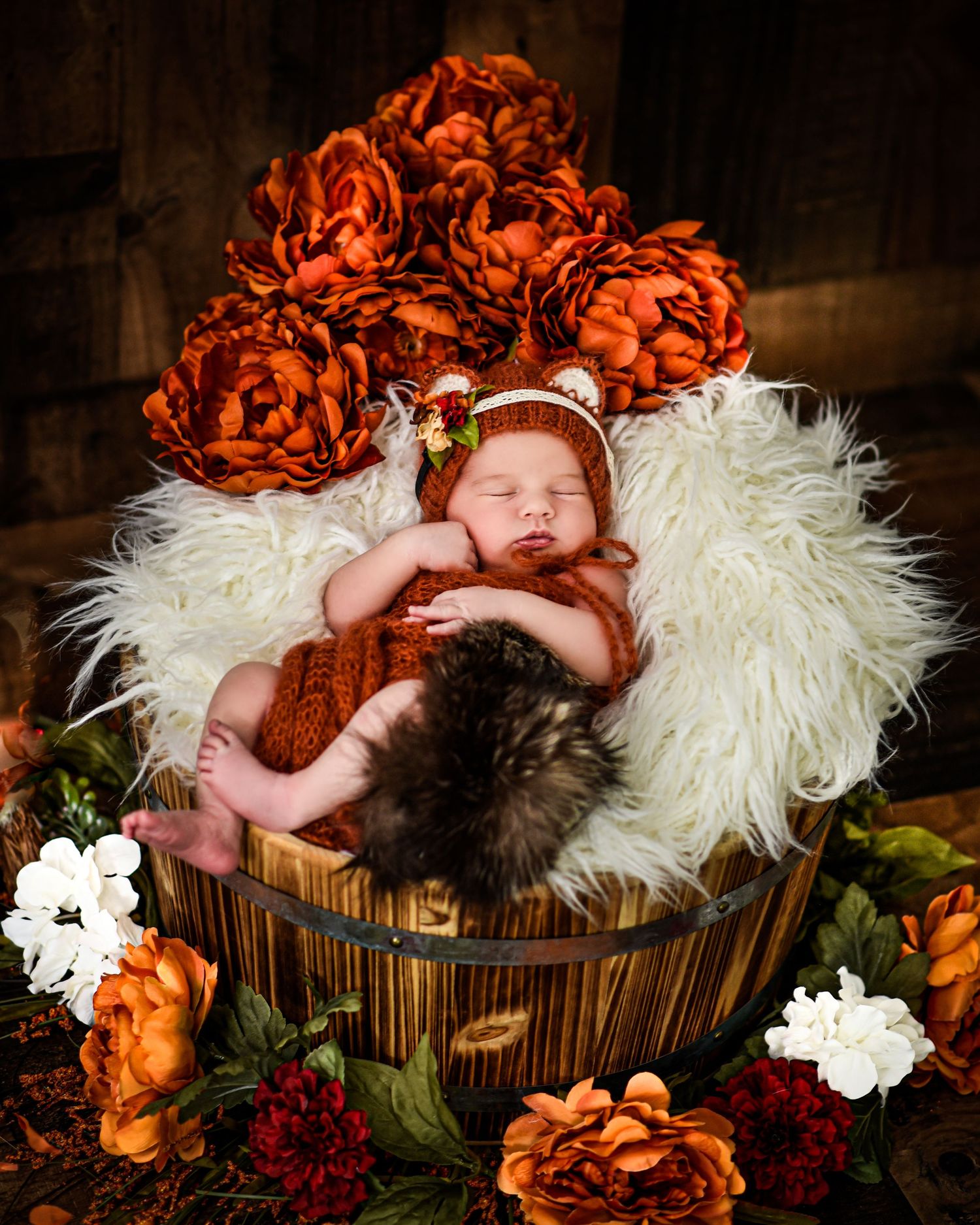 A newborn sleeps peacefully in a rustic wooden basket surrounded by orange and white floral decorations.
