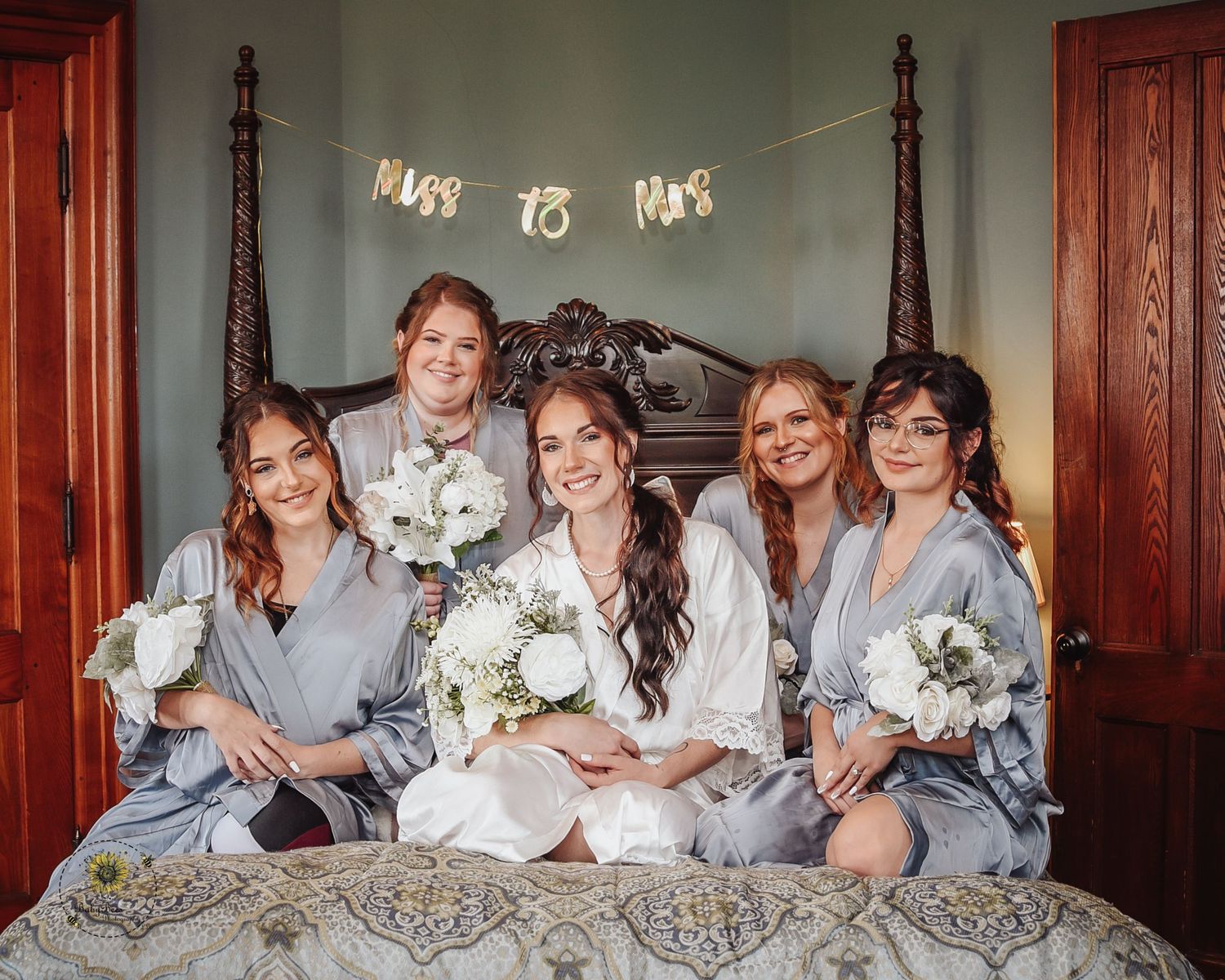 Wedding party in matching robes poses together on an elegant bed during pre-ceremony preparations.