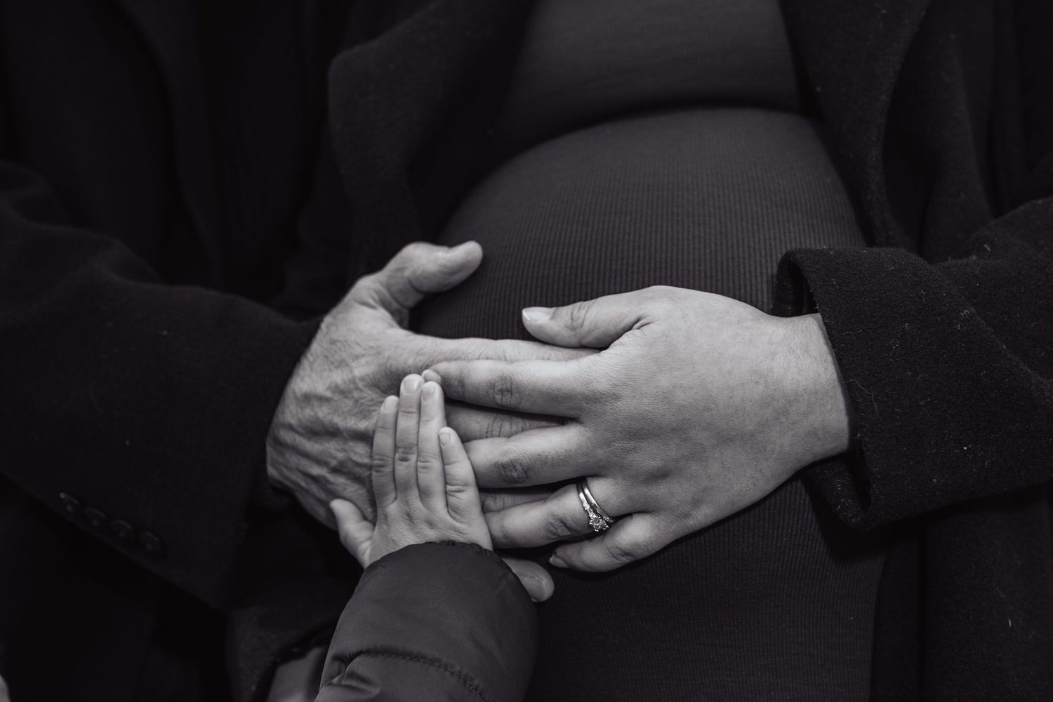 Black and white close-up image of hands with rings exchanging tender touch against dark background.