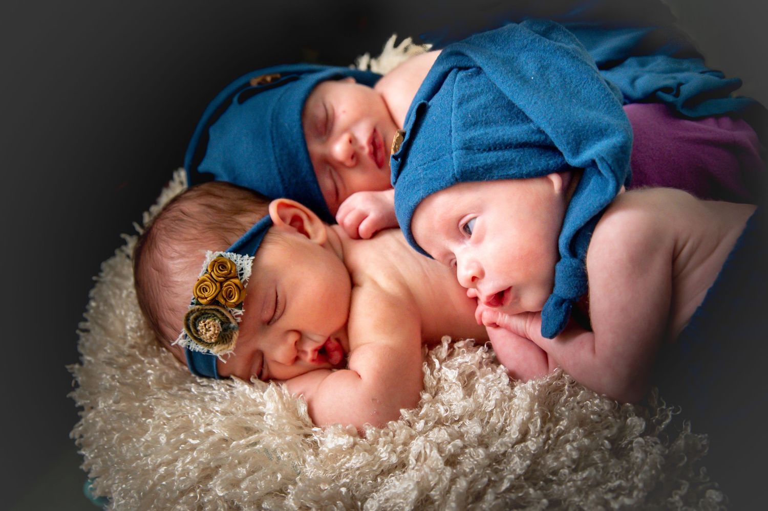 A sleeping baby in blue clothing lies on a white fluffy rug in a professional photography setting.