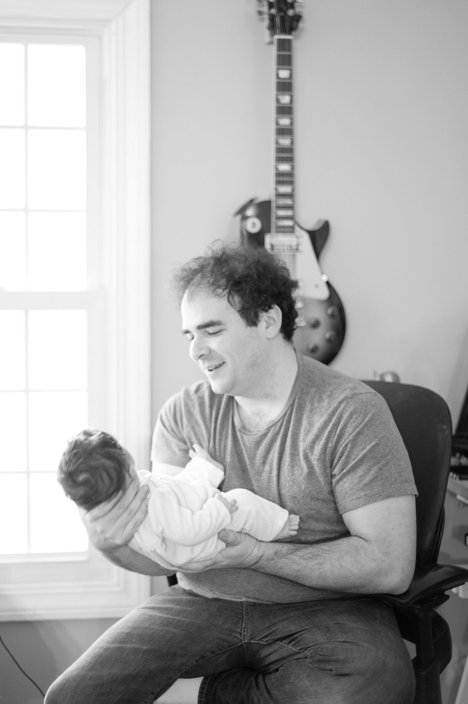 Parent in grey t-shirt sitting in chair and lovingly cradling a small baby in a series of tender moments.