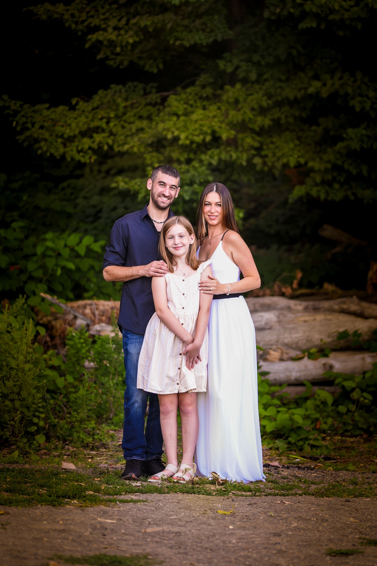 Family wearing coordinated white and navy outfits poses together in a natural outdoor setting with trees and rocks.