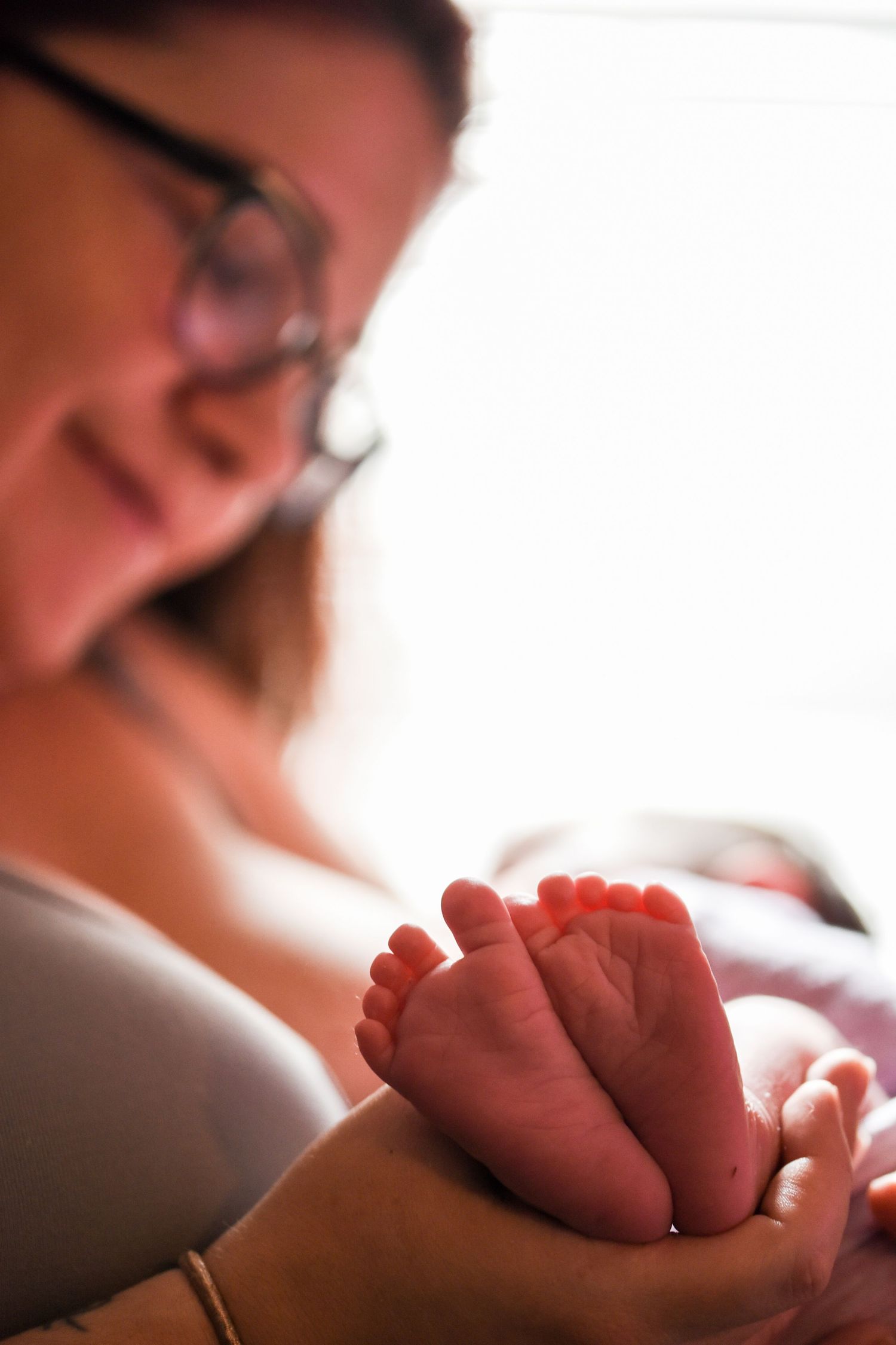 Close-up view of tiny newborn baby feet being gently cradled in adult hands in soft natural lighting.