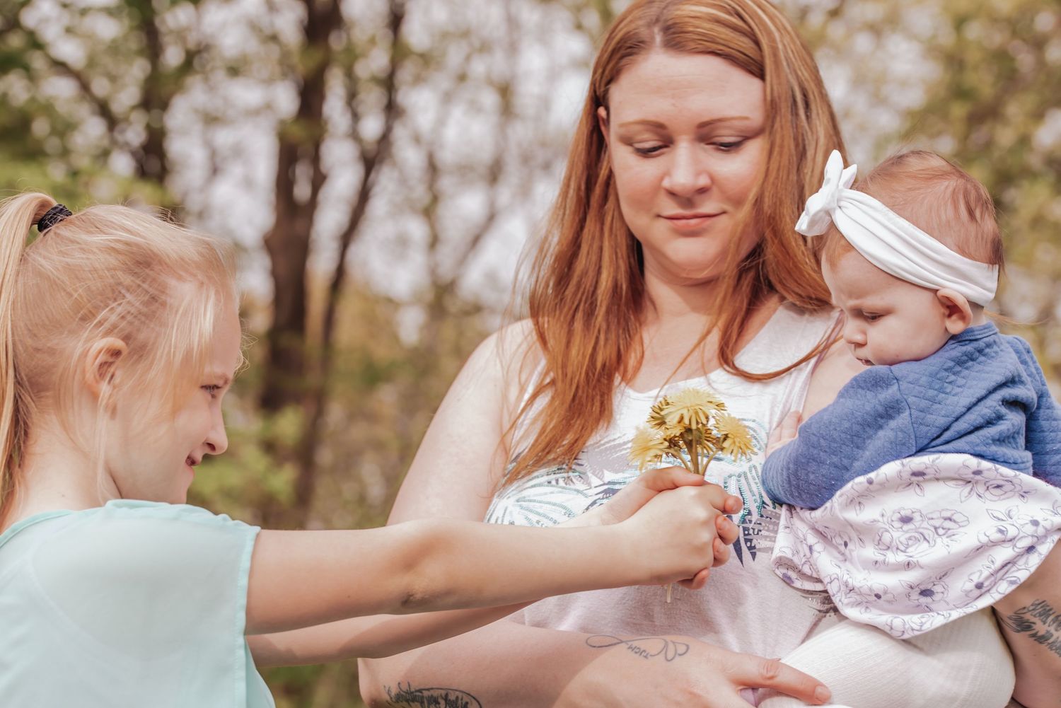 A family shares a tender moment outdoors as they look at yellow dandelion flowers together in spring.