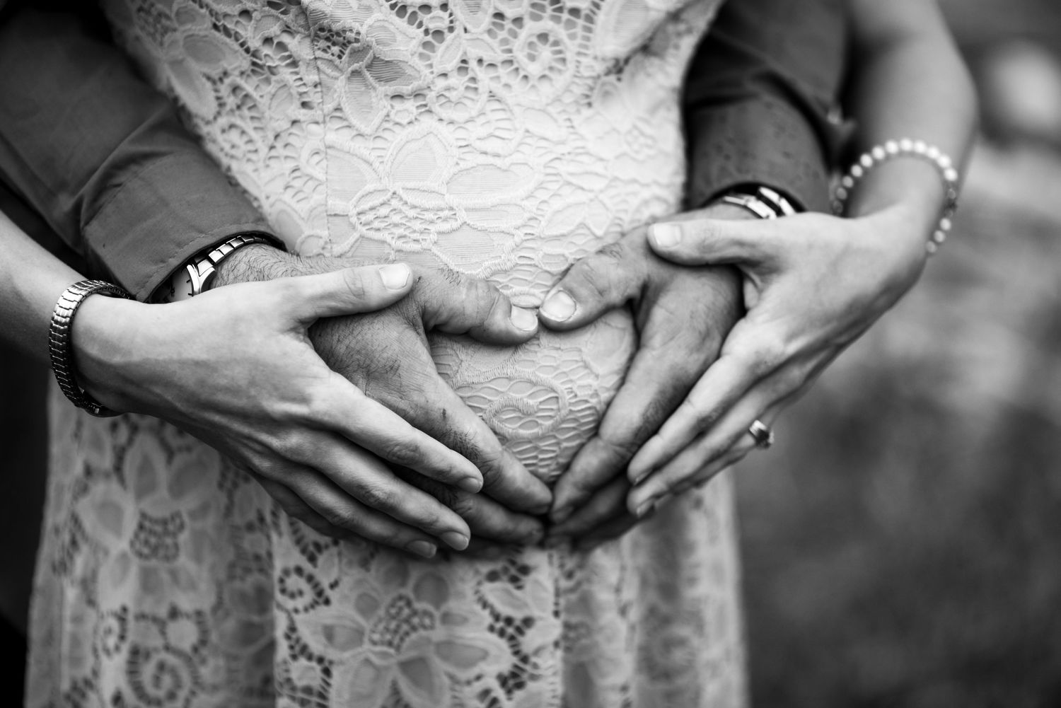 Black and white detail shots of hands clasped together against a white lace dress in a romantic wedding setting.