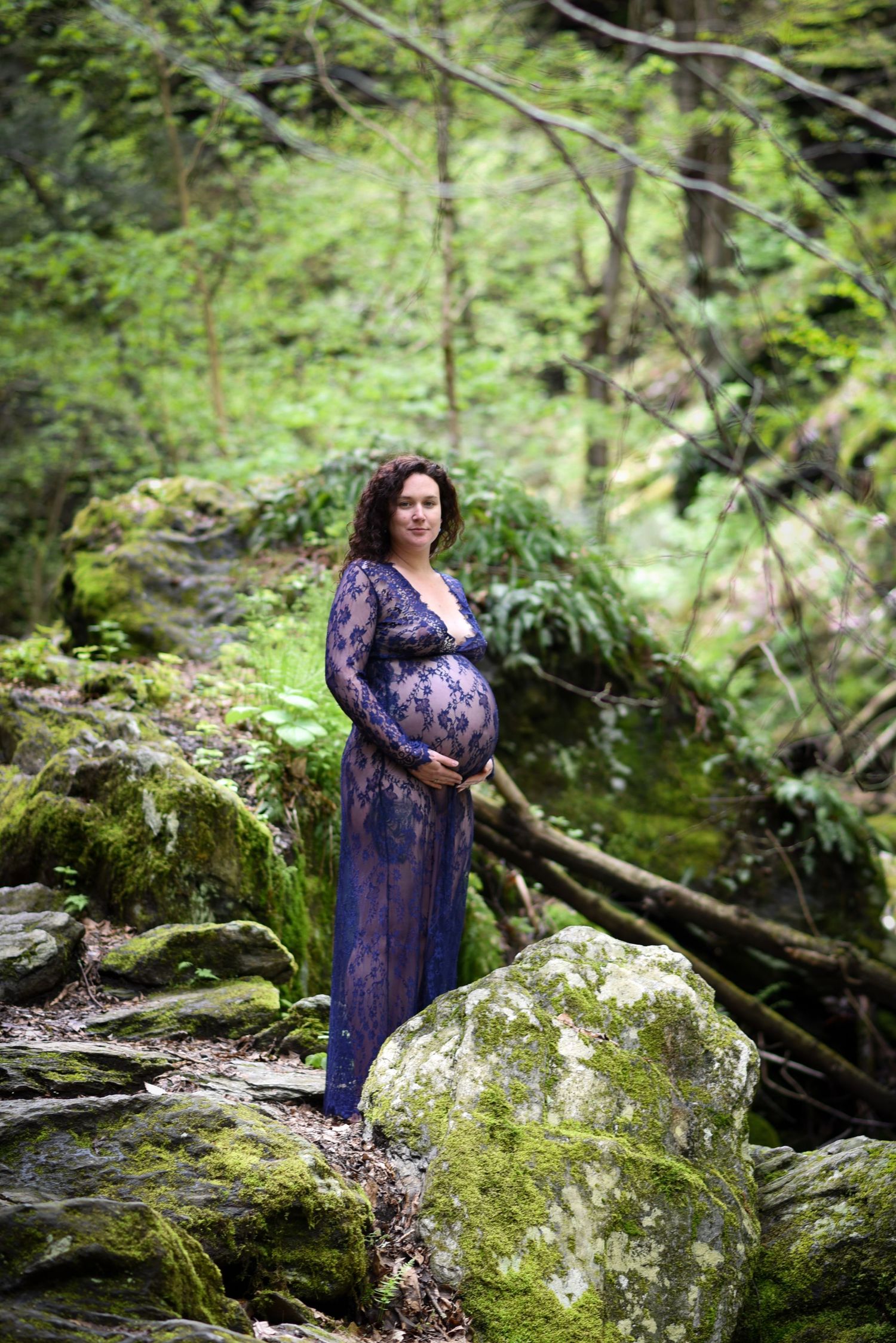 A figure in a purple floral dress poses gracefully among moss-covered rocks and lush forest greenery.