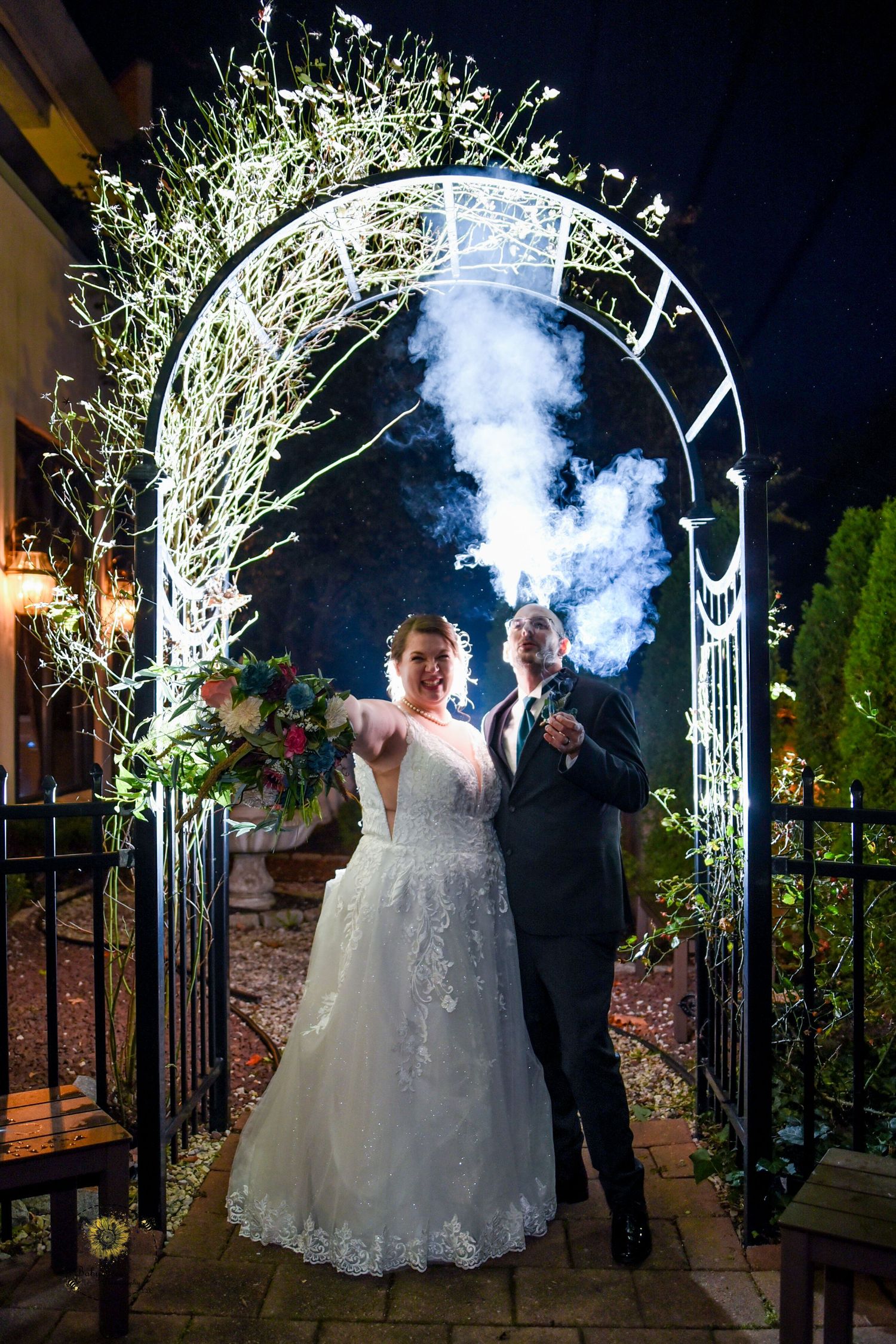 Nighttime wedding photos under lit archway with smoke effects creating dramatic atmosphere.