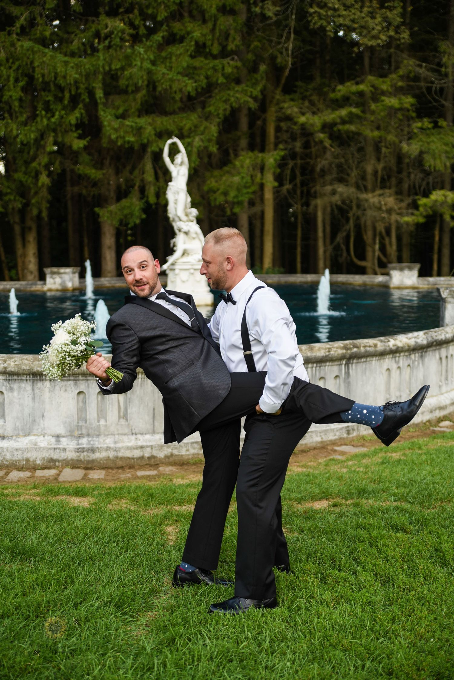 Groomsmen performing synchronized leg kicks on grass during fun wedding photo shoot.