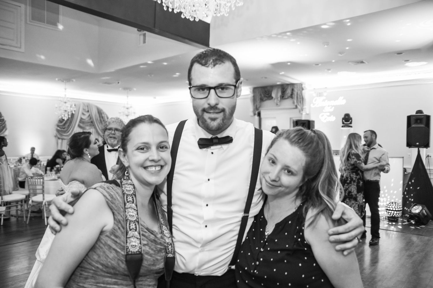 Wedding guests enjoying festivities in a reception hall with chandelier lighting.