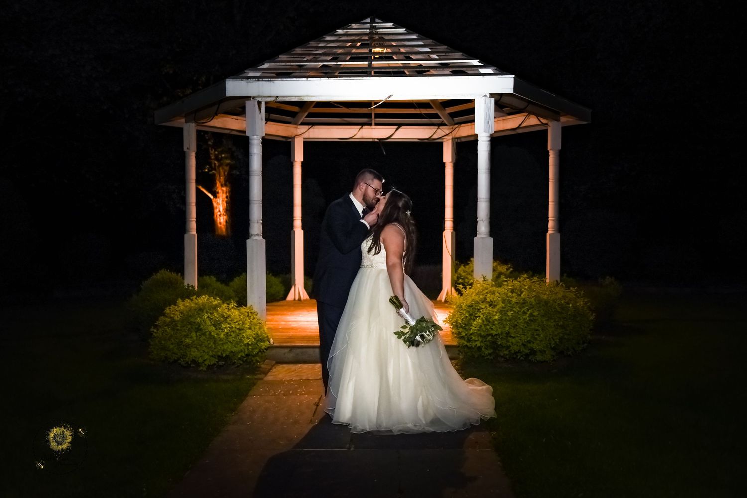 Romantic wedding couple silhouetted against glowing lights in a nighttime outdoor setting.