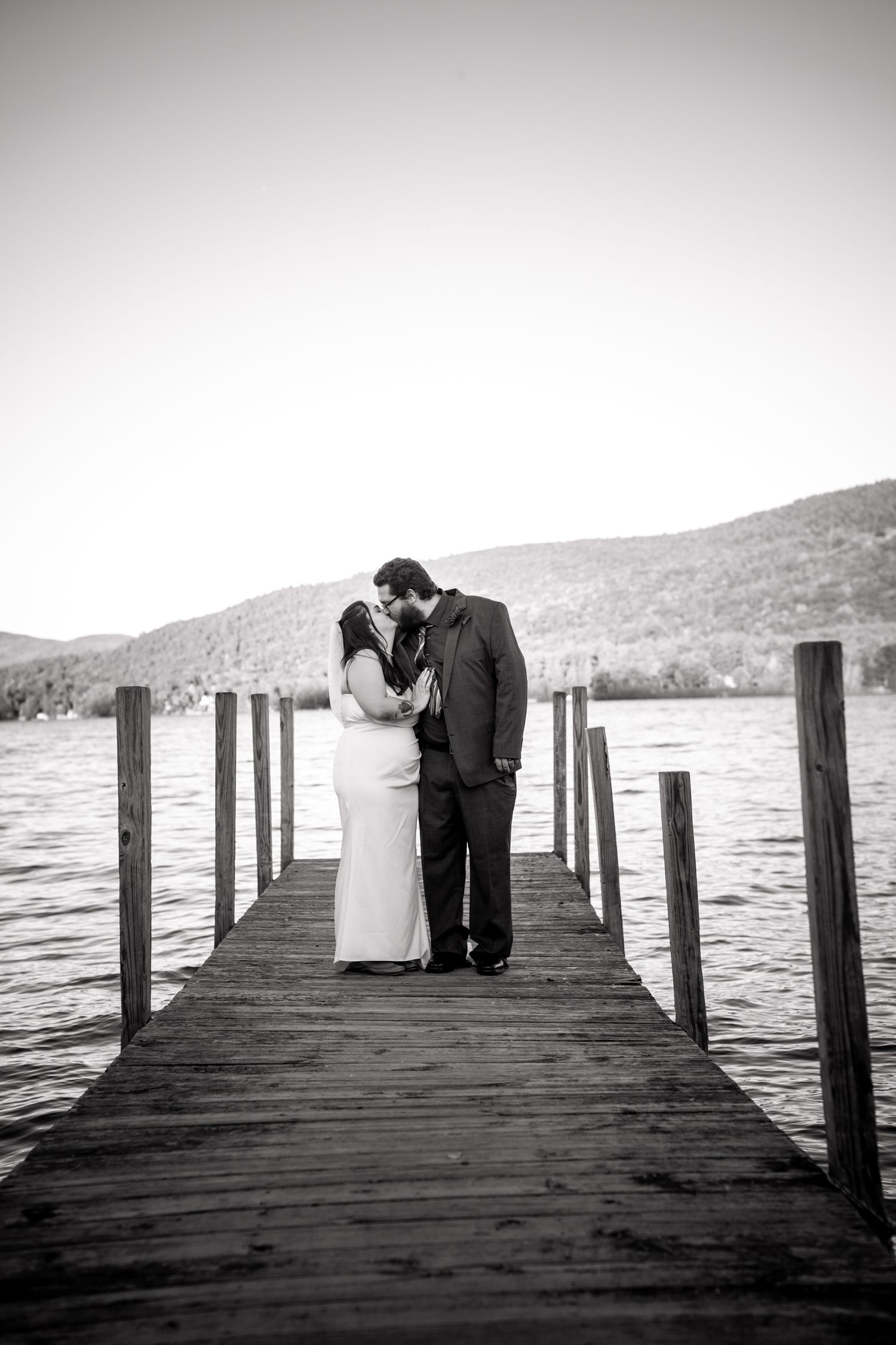A romantic black and white portrait of newlyweds on a wooden dock over a lake.