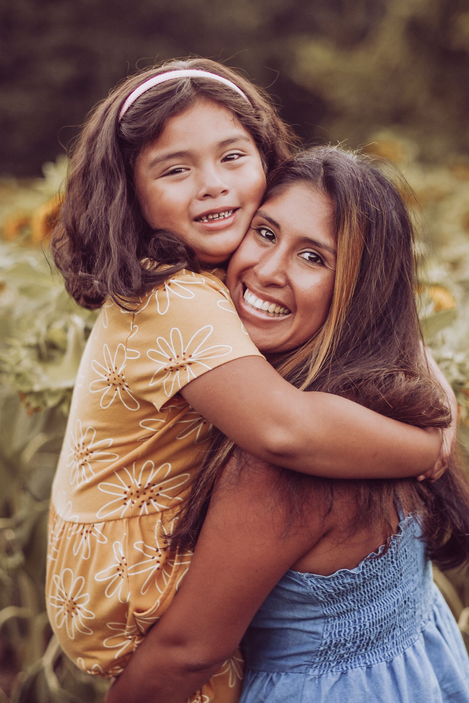 Two people share a joyful embrace while wearing a yellow floral dress and blue top in an outdoor setting.