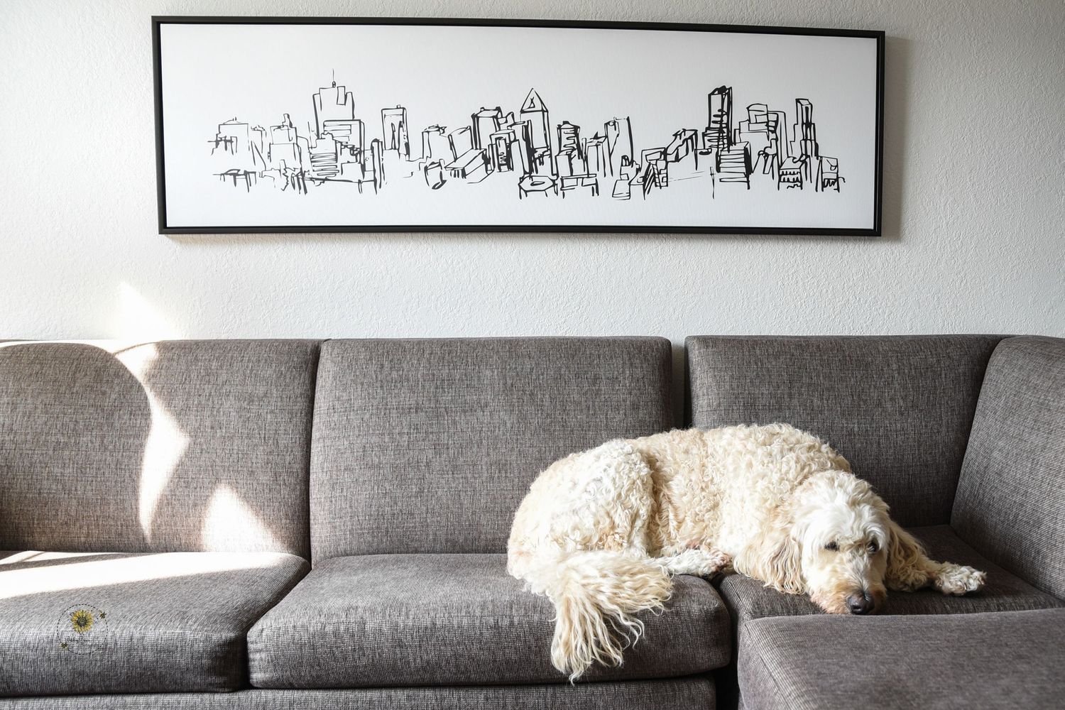 Modern cityscape artwork hanging above grey couch with white throw pillows.