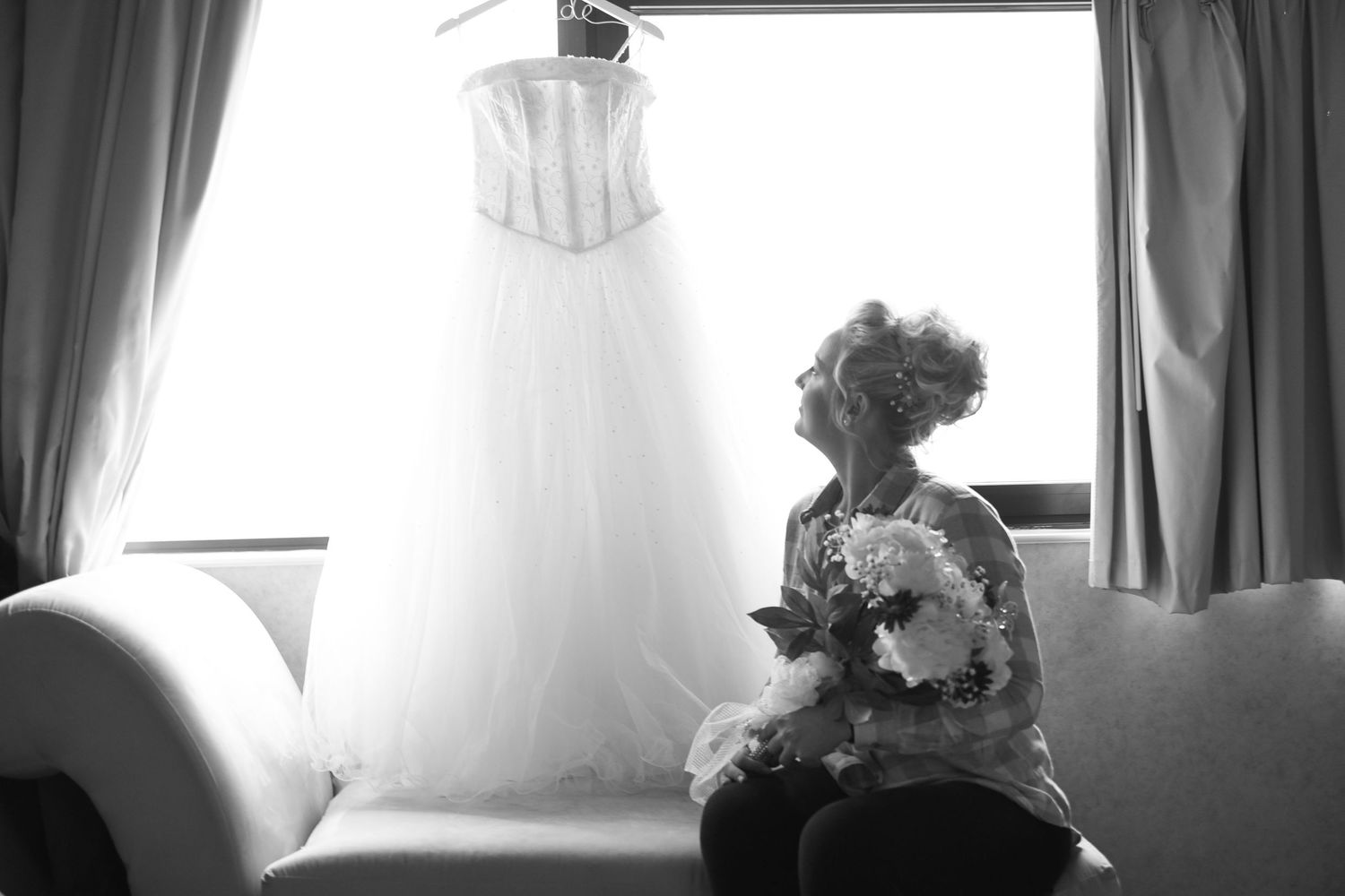Wedding dress hanging in window with elegant lace details and flowing white fabric.