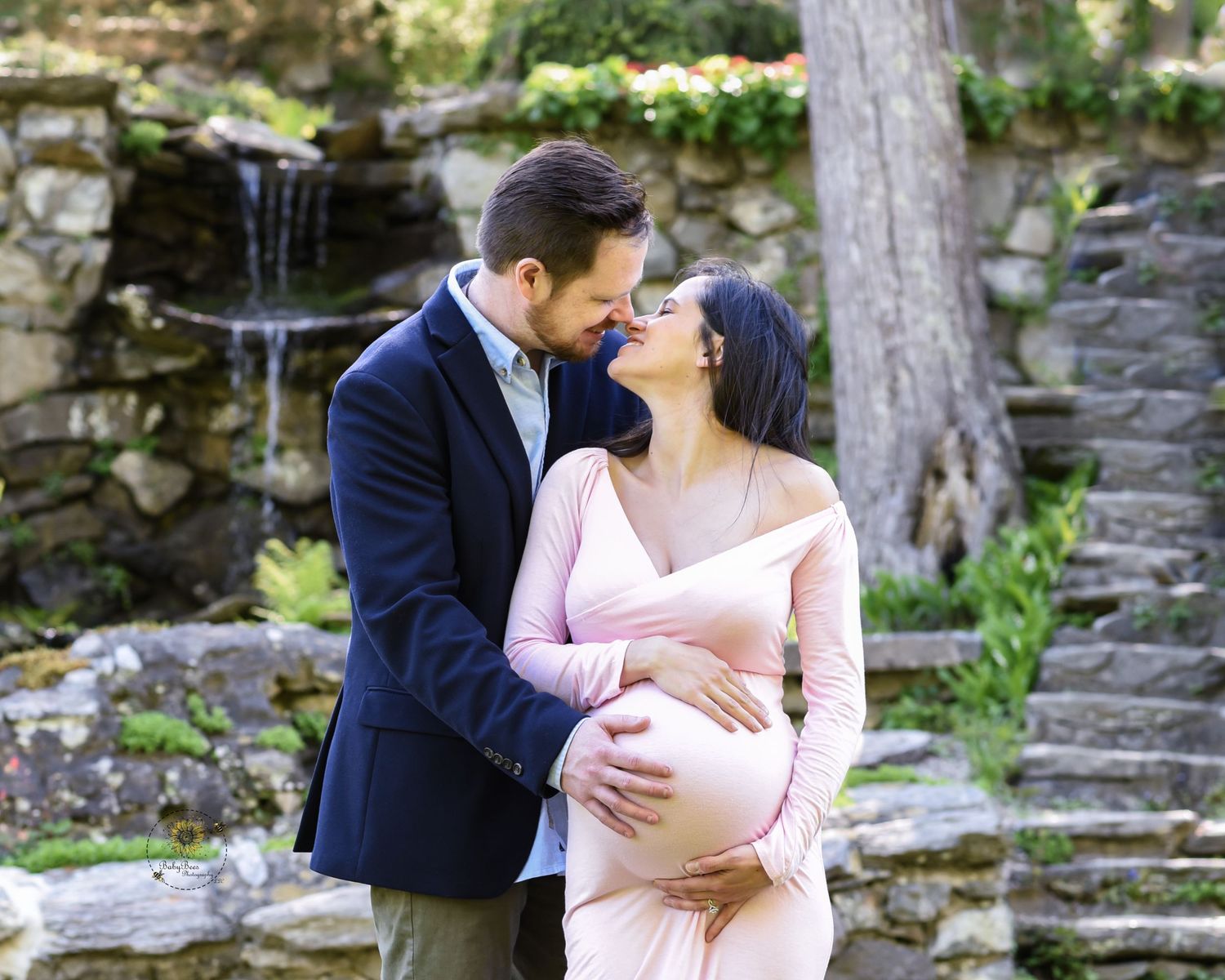 A romantic couple in formal attire embrace near stone steps in a lush garden setting during a photo session.