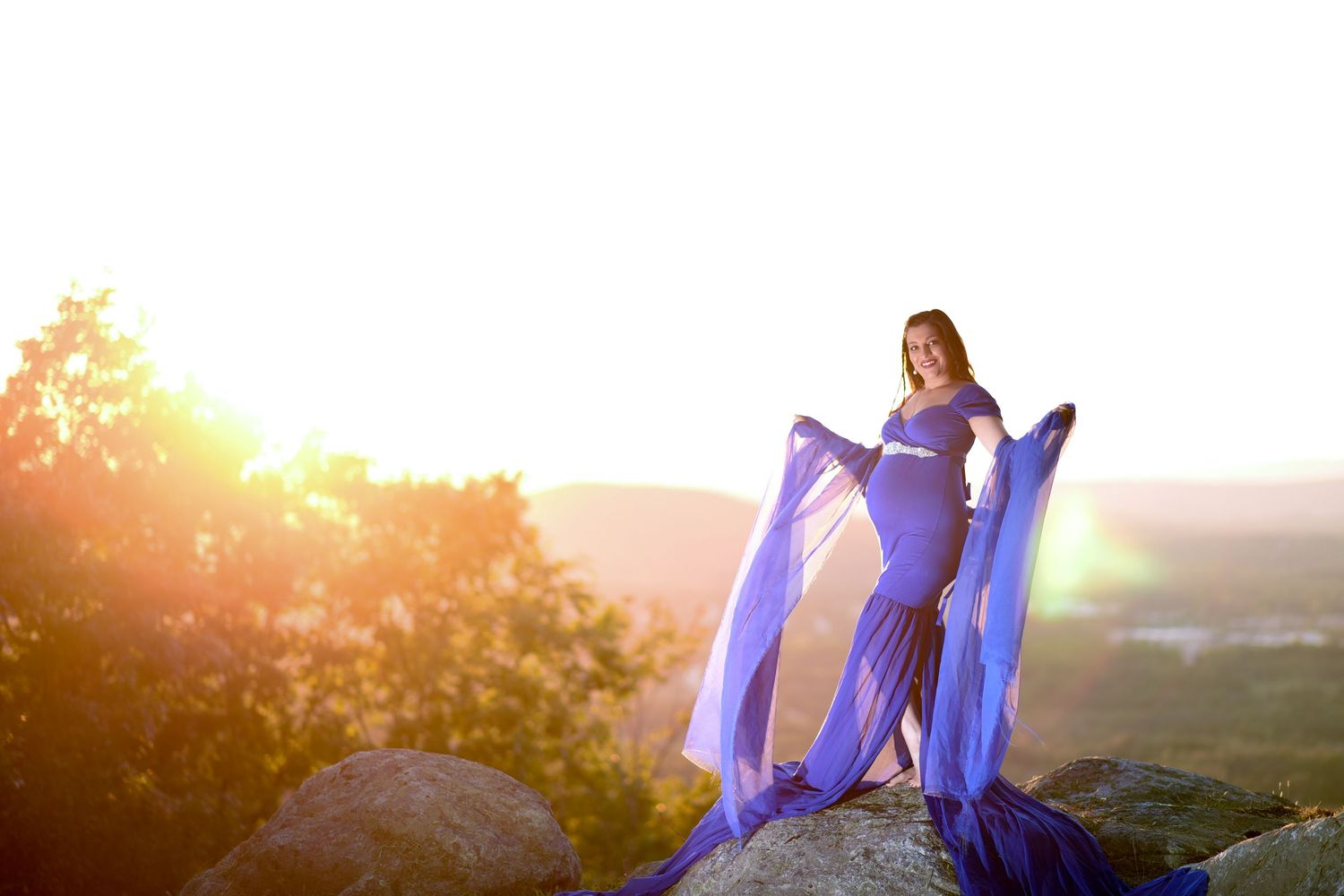 A person in a flowing purple dress stands on a hilltop at sunset creating a dreamy silhouette against the golden sky.