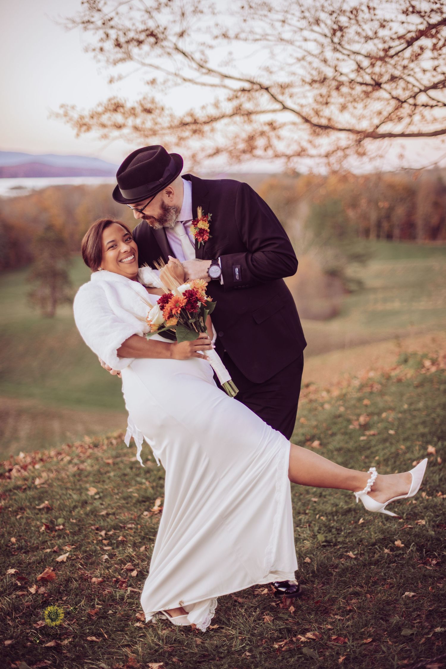 Playful wedding couple poses in white dress and black suit on an autumn hillside.