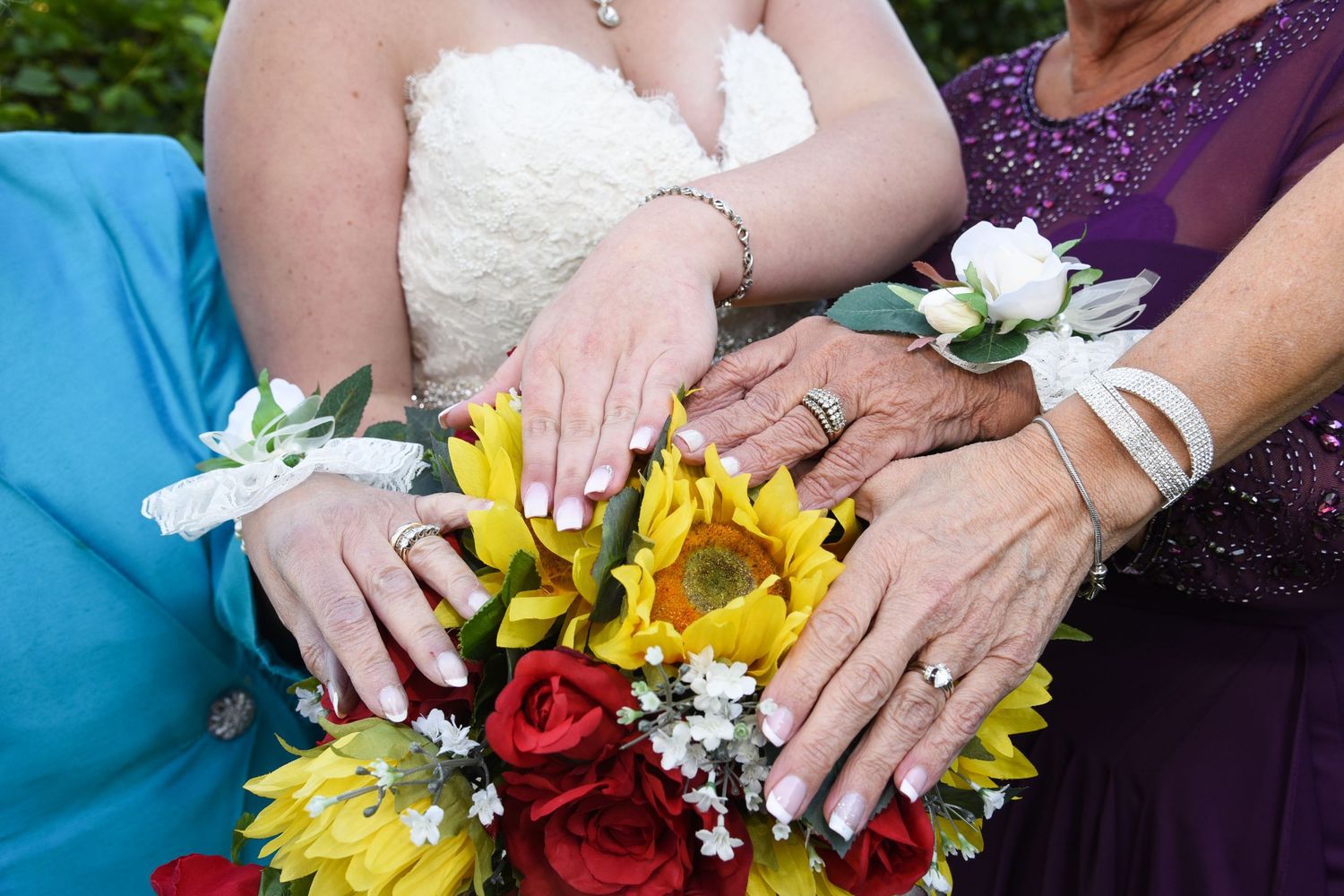 Close-up of hands holding colorful wedding bouquets with yellow and red flowers.