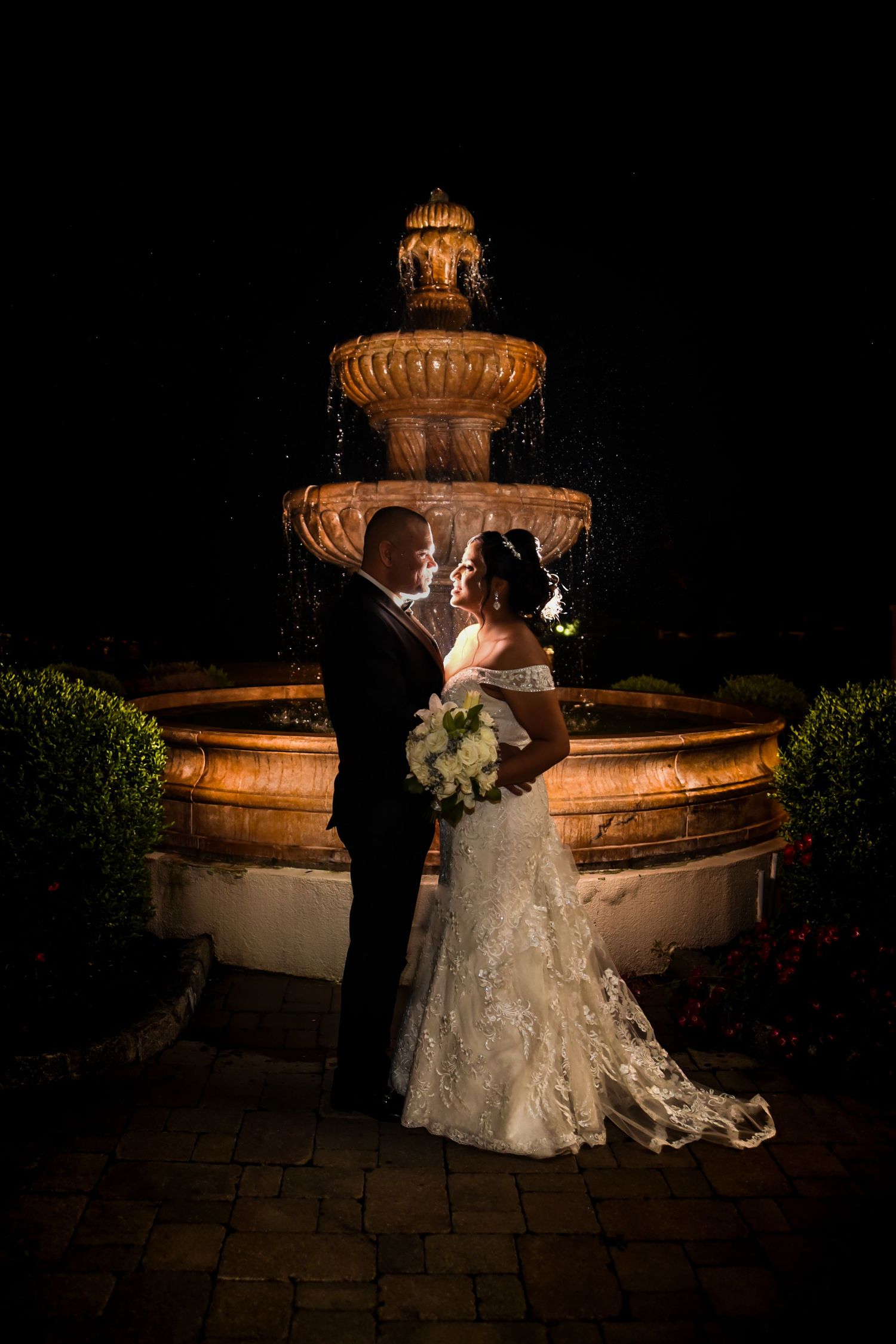 Romantic nighttime wedding portrait by an illuminated stone fountain.