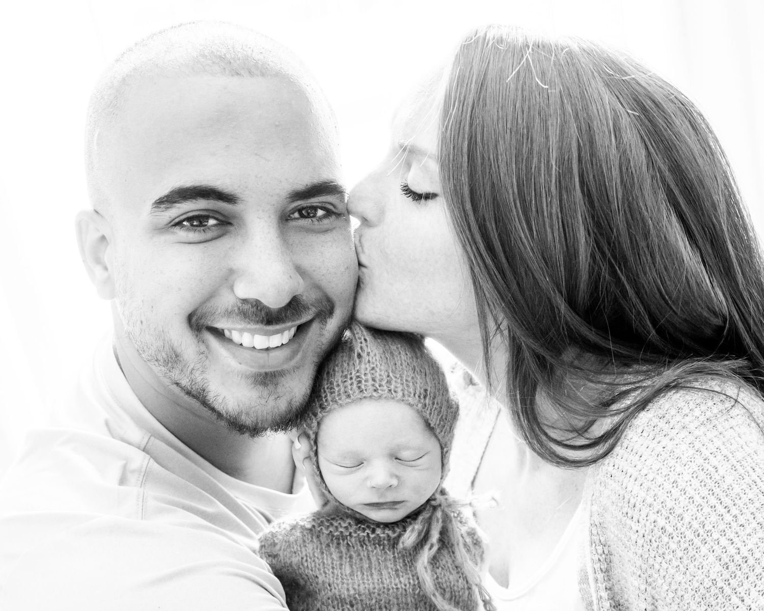 Black and white portrait of parents with their newborn baby wearing a knit sweater.