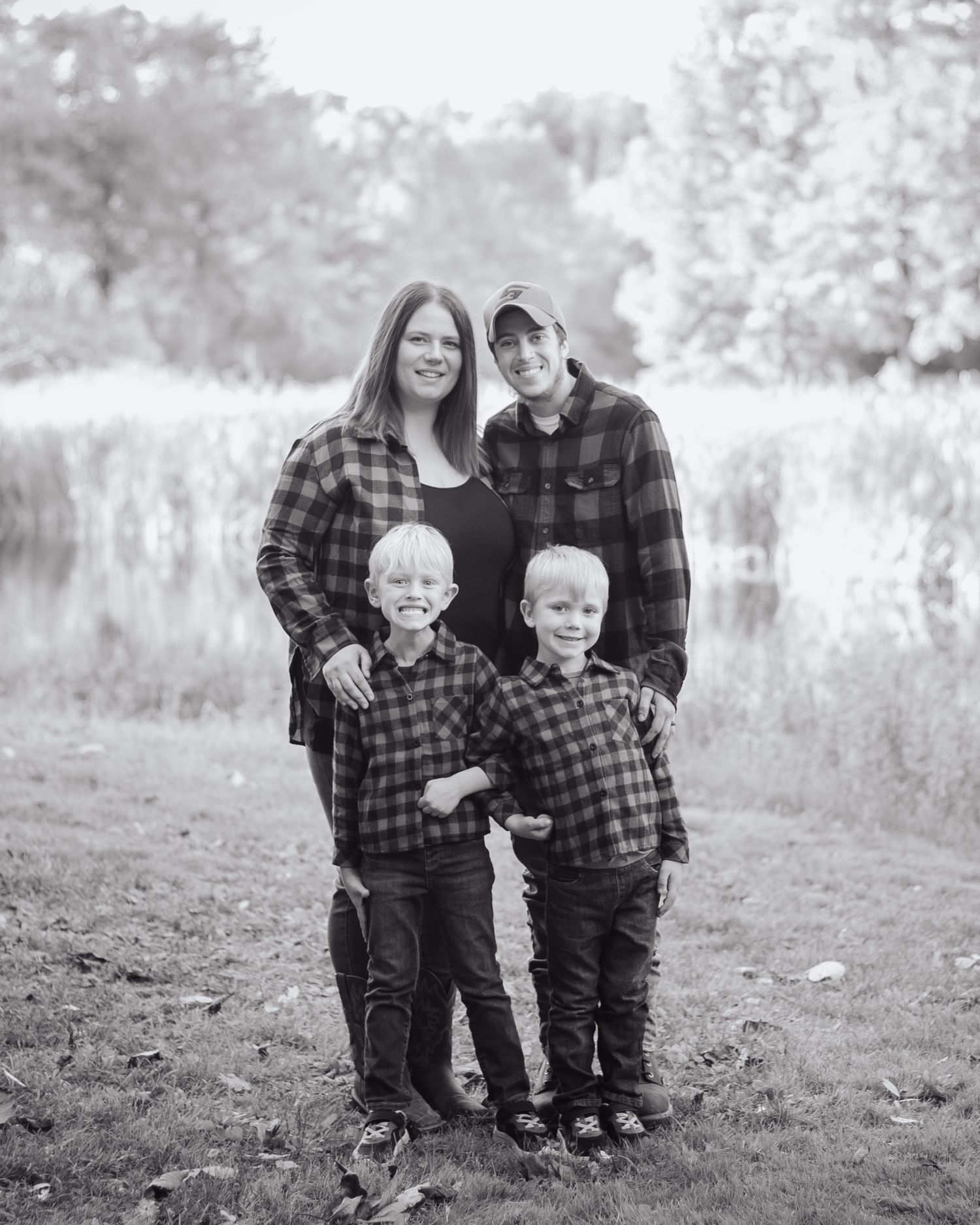 A family of four wearing matching plaid flannel shirts poses together outdoors in a black and white portrait.