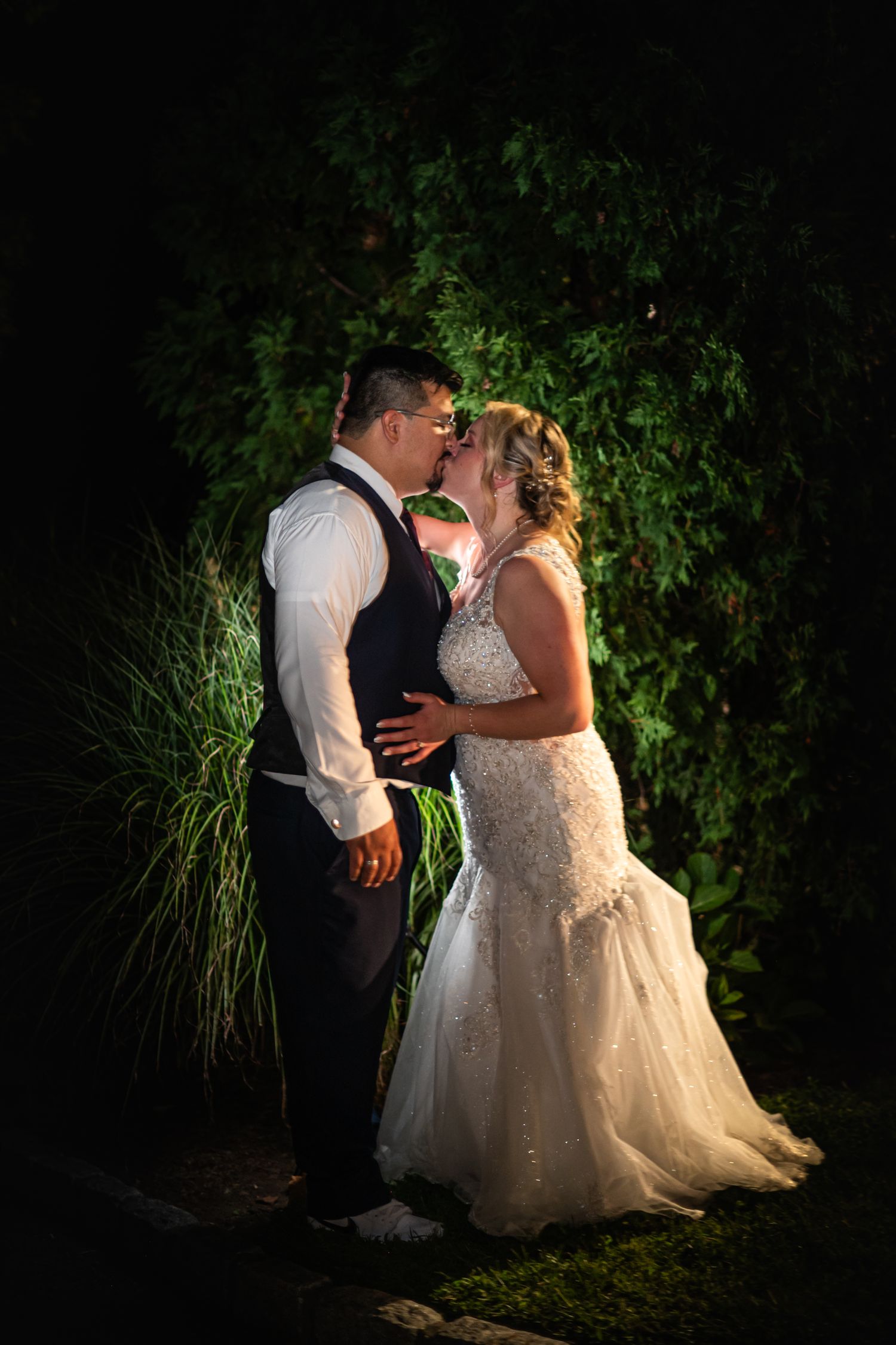 A dramatic nighttime portrait of newlyweds embracing against dark foliage.