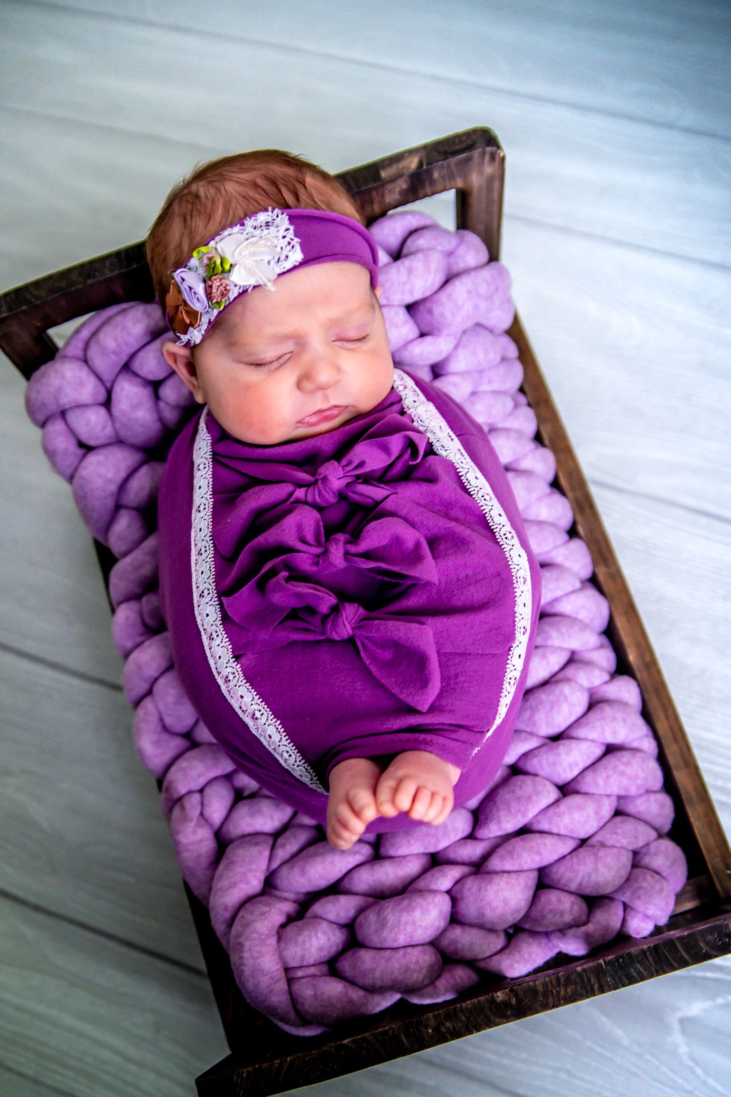 Sleeping baby wrapped in purple swaddle rests on chunky knit purple blanket with matching headband.