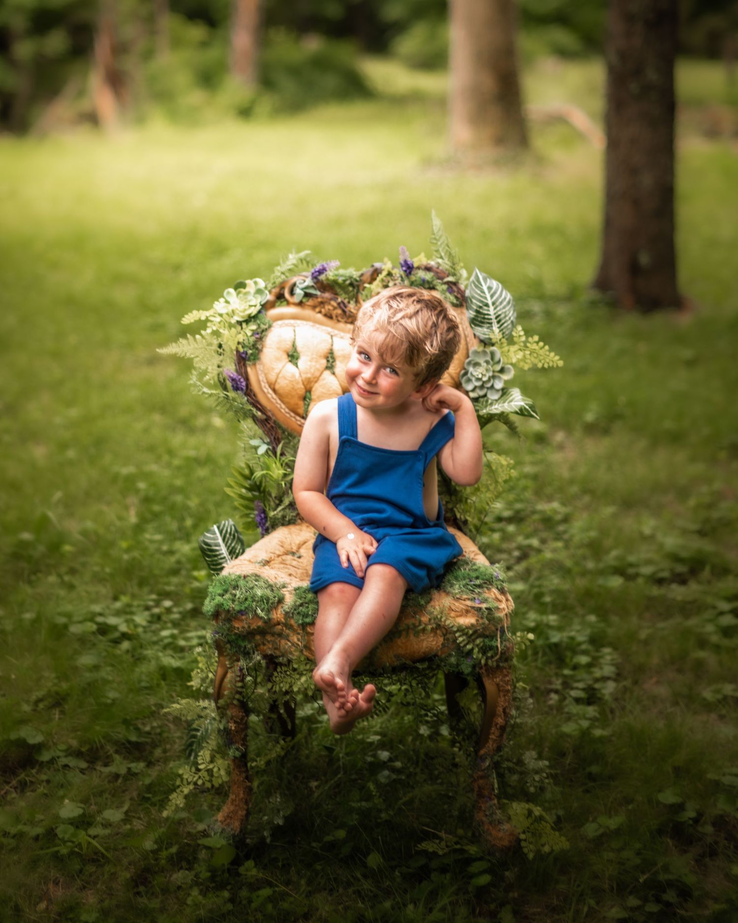 Child sitting in a decorative chair surrounded by greenery in a sunny garden setting.