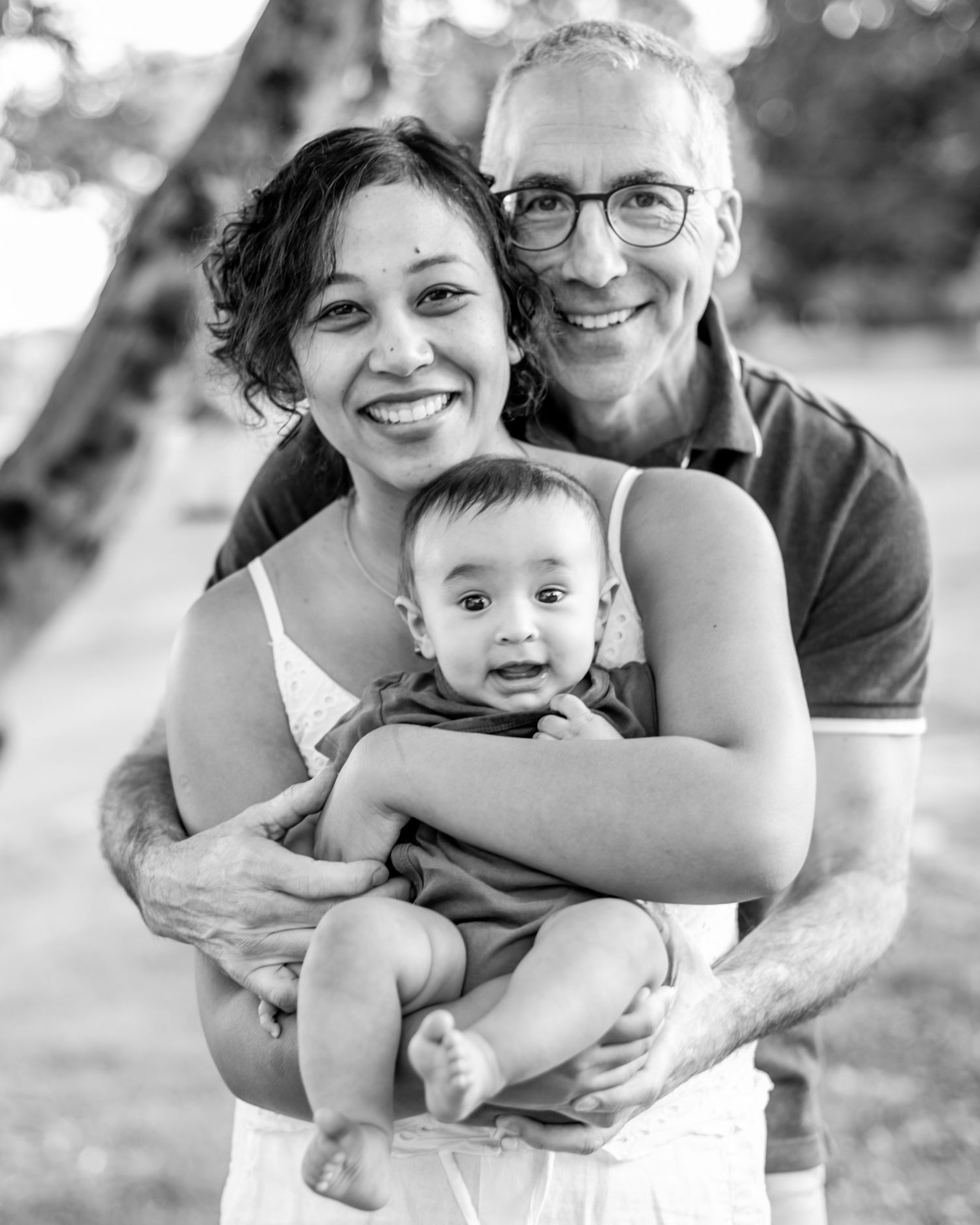 A black and white portrait of a happy family embracing outdoors with their baby.