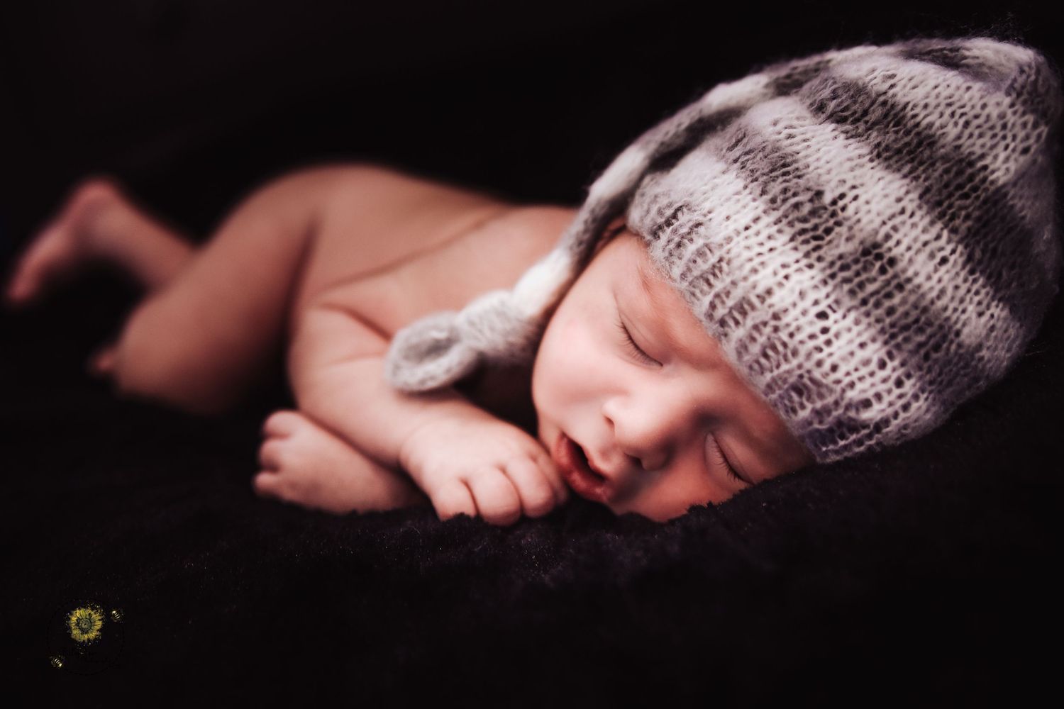 Sleeping newborn wearing knitted gray beanie hat in dark moody portrait.