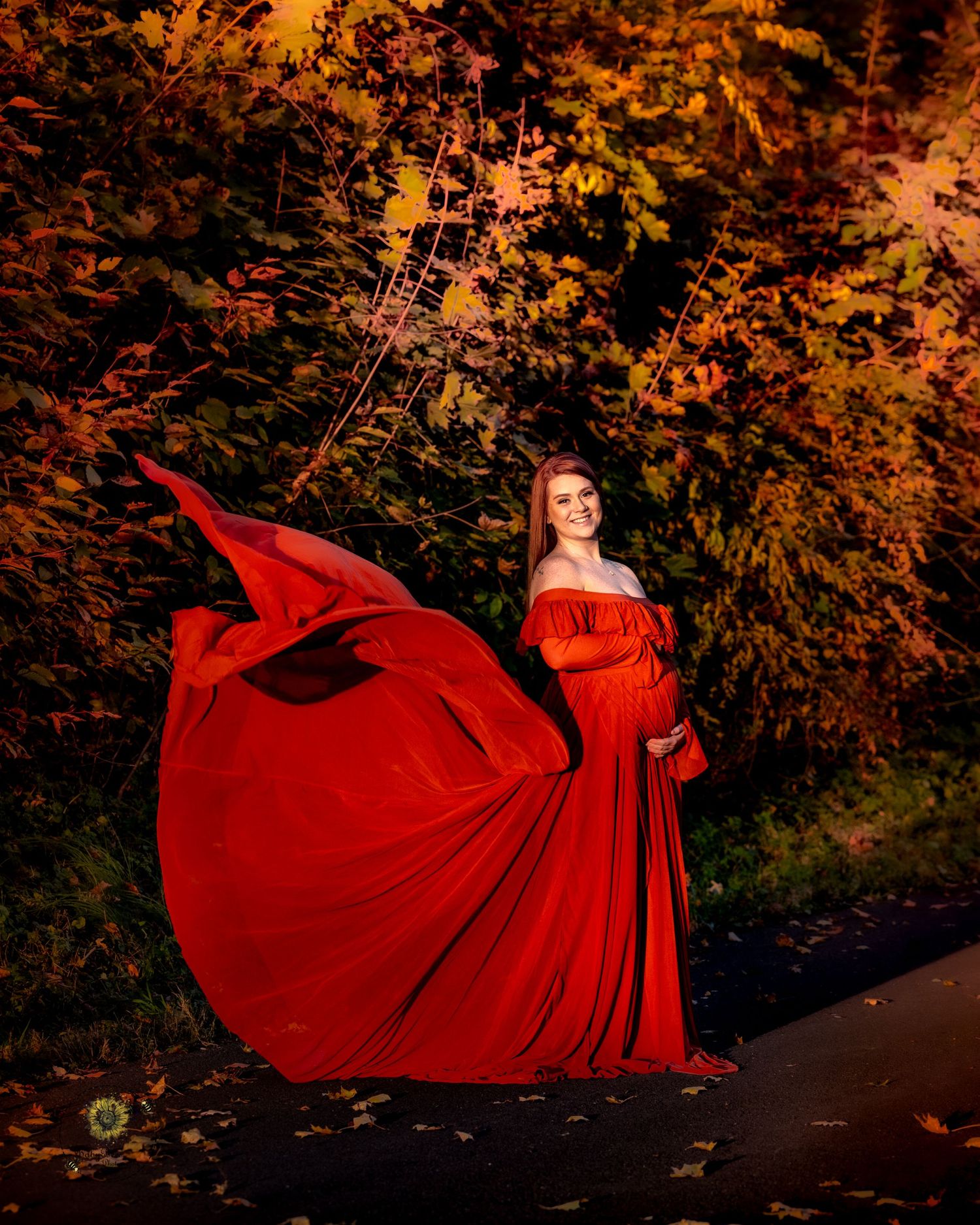 A flowing red dress billows dramatically against an autumn forest backdrop in golden evening light.