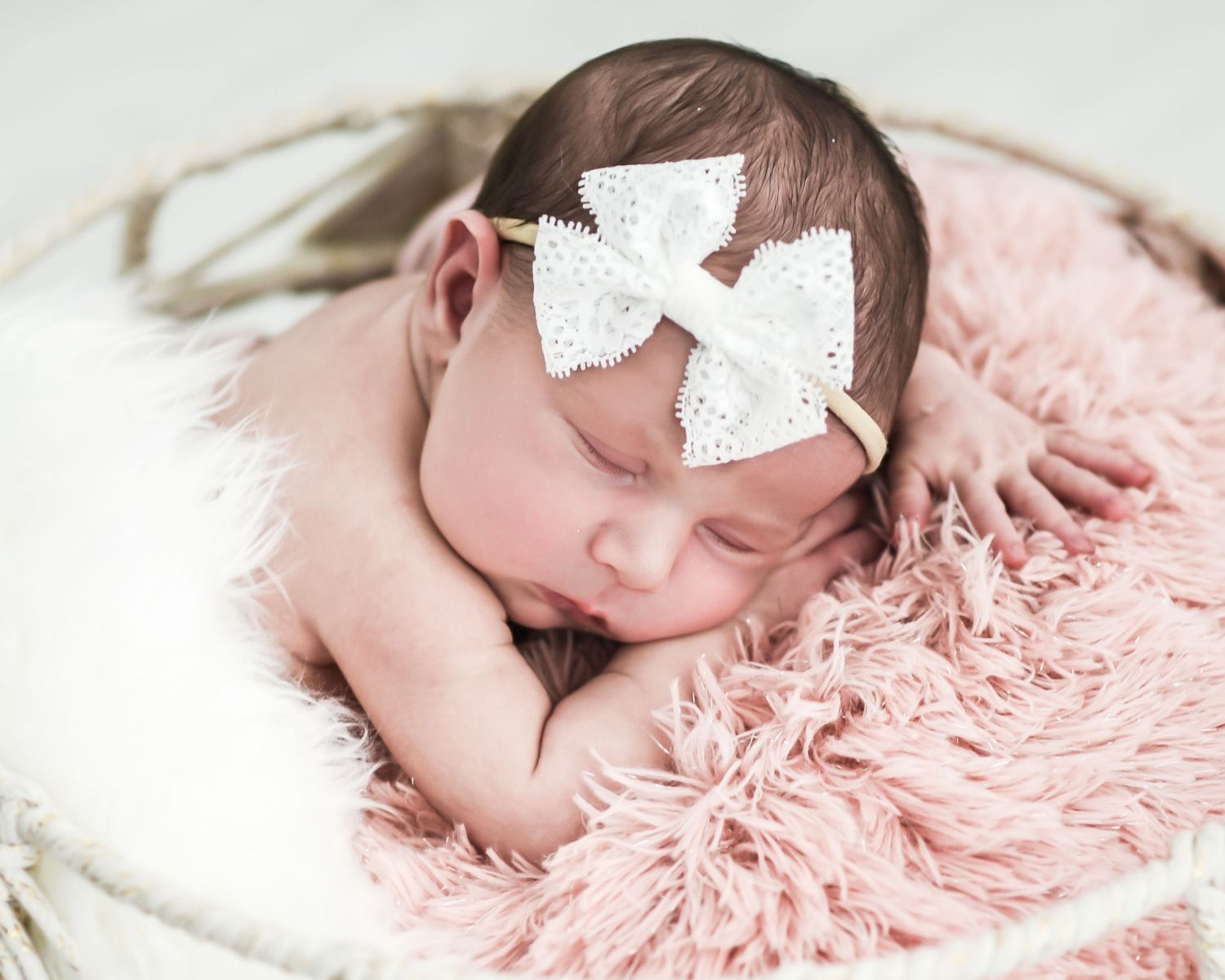 Newborn baby sleeping peacefully on soft pink fur blanket in delicate white headband.
