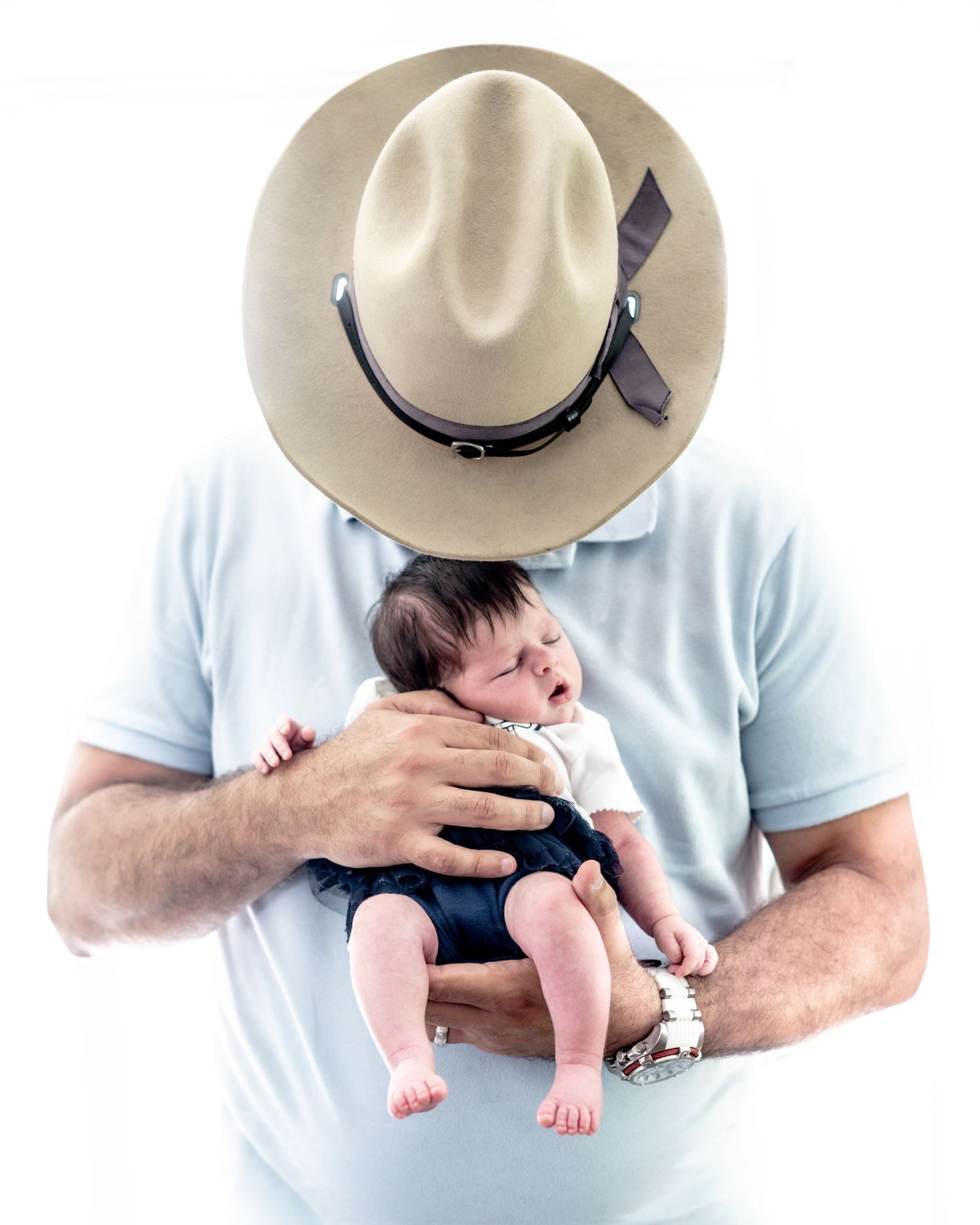 A person wearing a light cowboy hat and blue shirt holds a small baby in their arms.