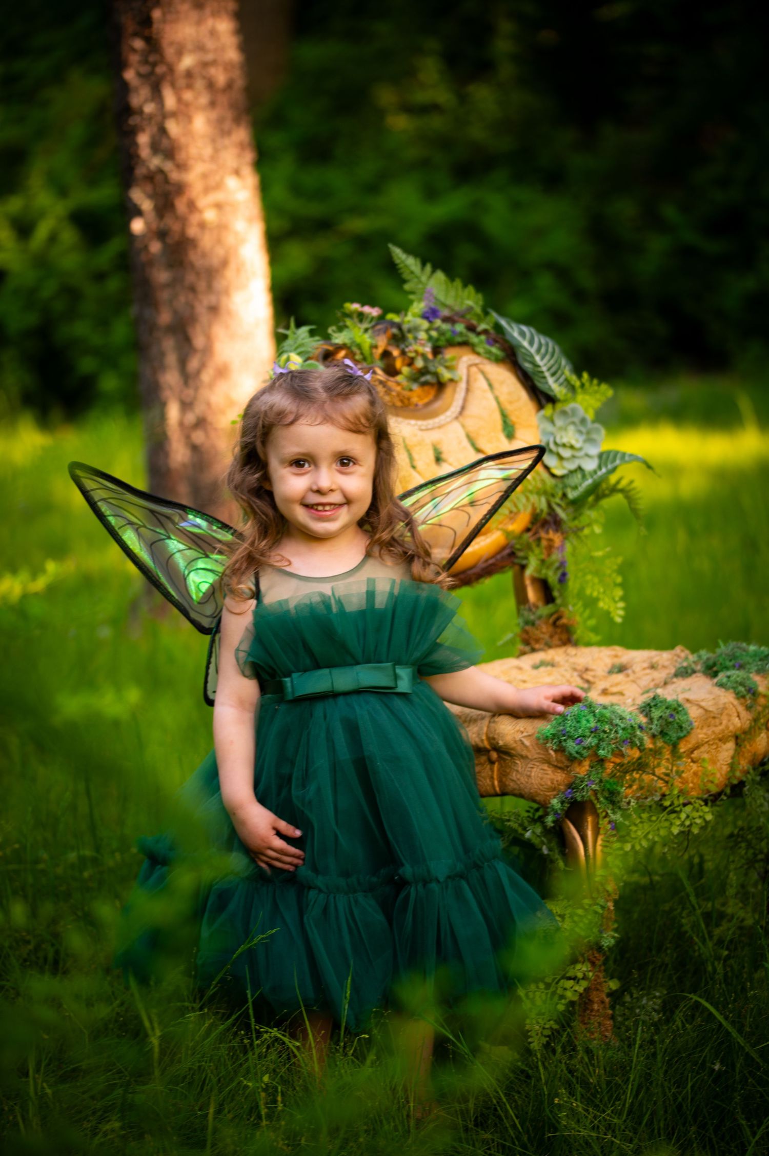 A magical fairy garden scene with an enchanted green tulle dress and decorative wings amid lush outdoor greenery.