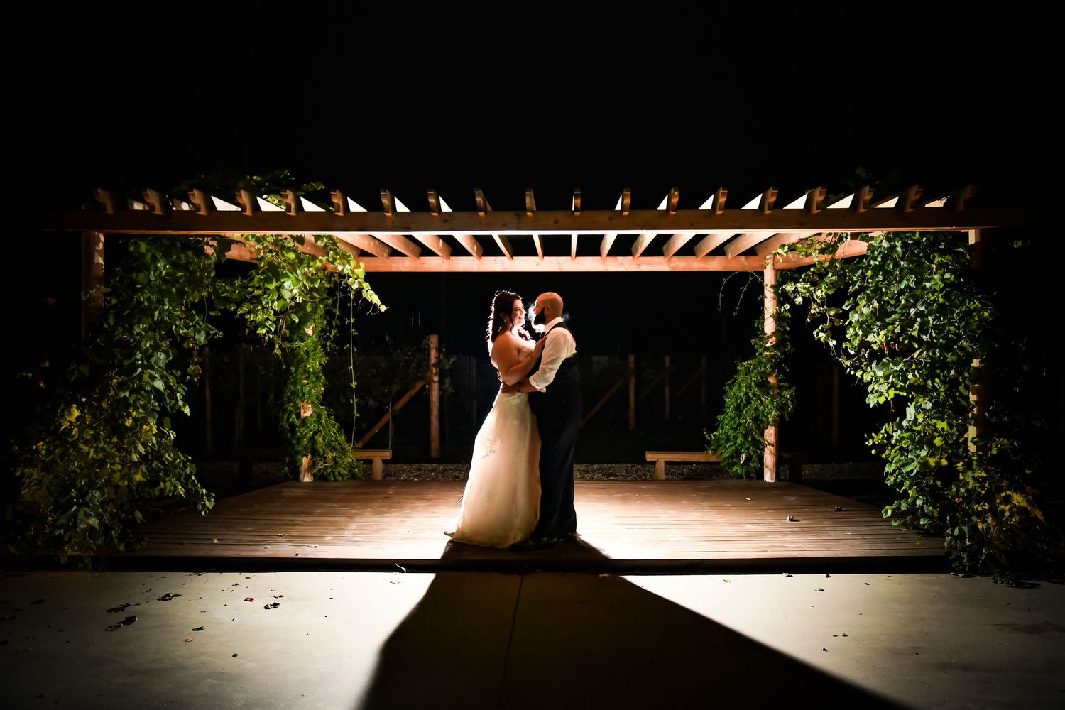 Dramatic backlit silhouette of a couple under a pergola during an evening wedding.