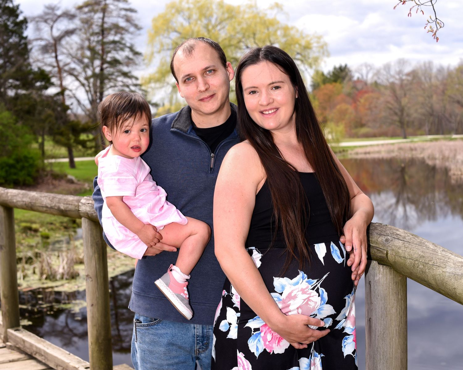 A family stands together on a wooden bridge overlooking a serene pond during autumn.