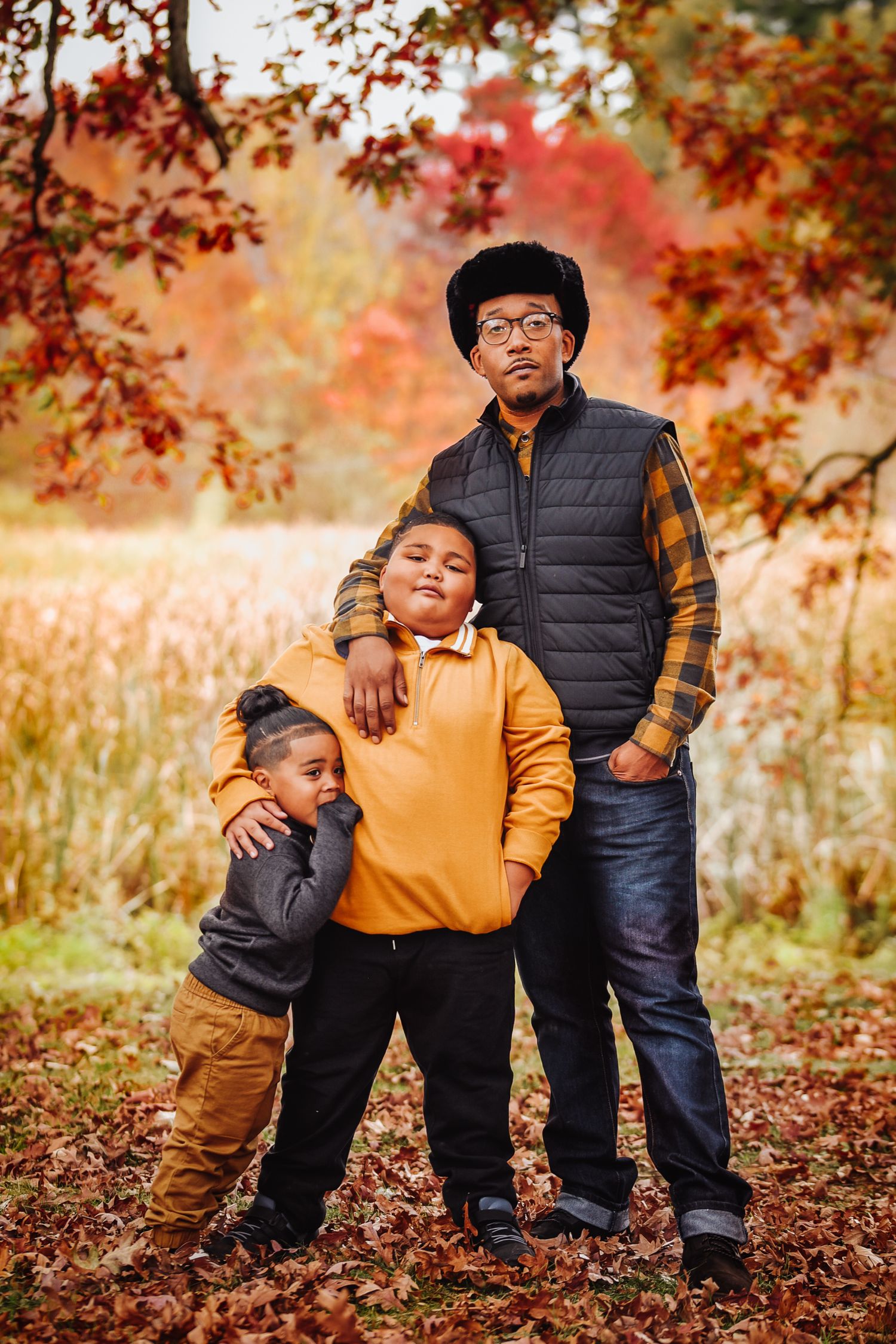 Three people in coordinating yellow and black outfits pose together on autumn leaves during a fall photo session.