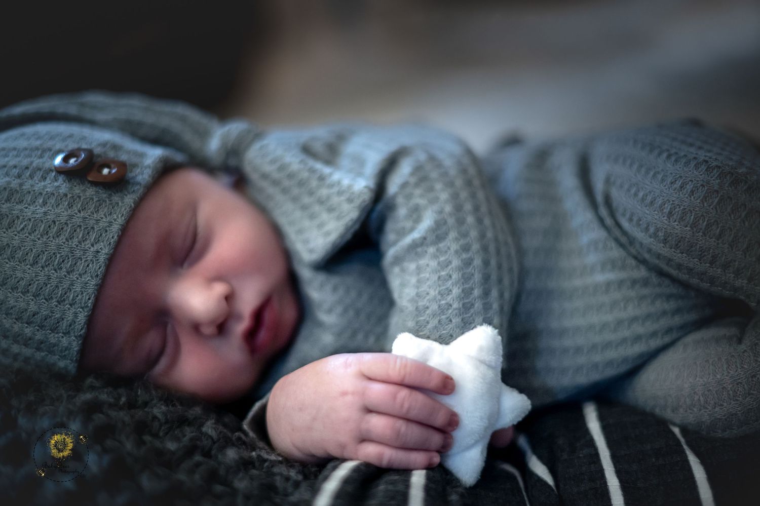 Sleeping baby in soft blue knit sweater holding white toy against dark background.